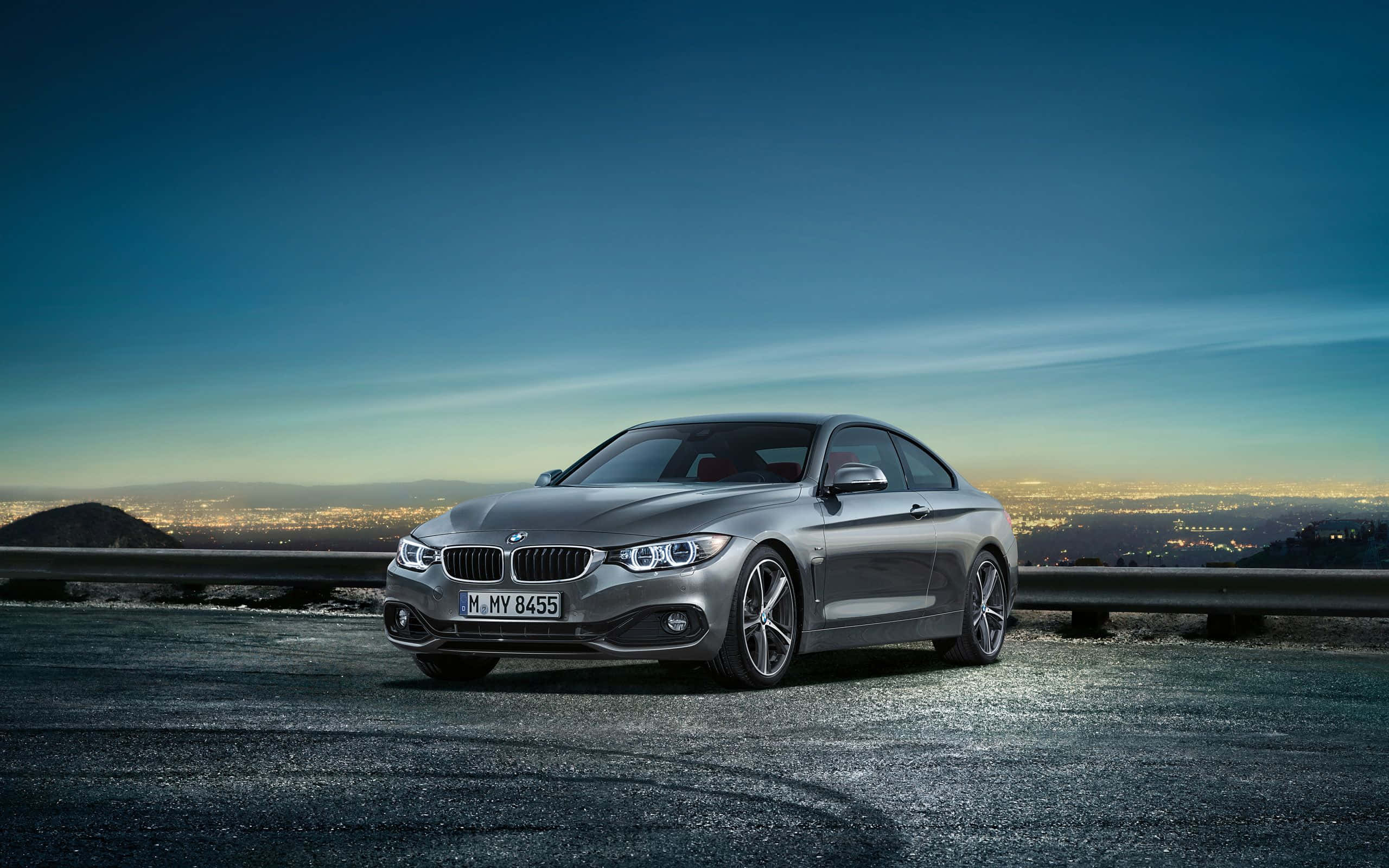 Bmw 4 Series 桌布 壁紙 — 一輛時尚的銀色BMW雙門跑車停泊在黃昏的山路上，下方是閃爍的城市景觀。