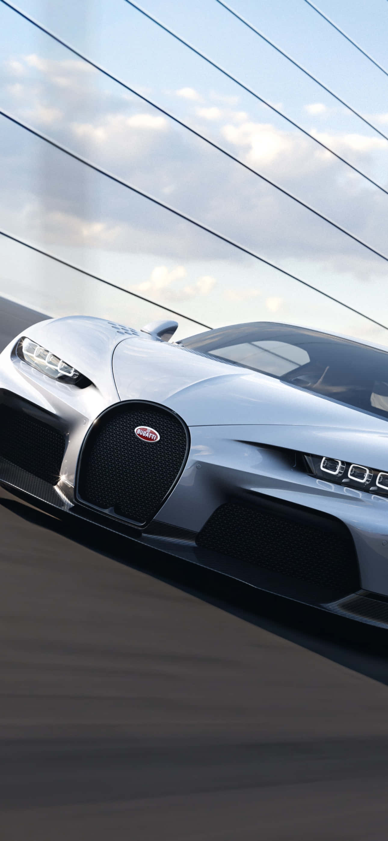 Bugatti Phone 桌布 壁紙 — 一輛時尚的銀色Bugatti超跑在多雲的天空下沿著現代玻璃橋疾馳。
