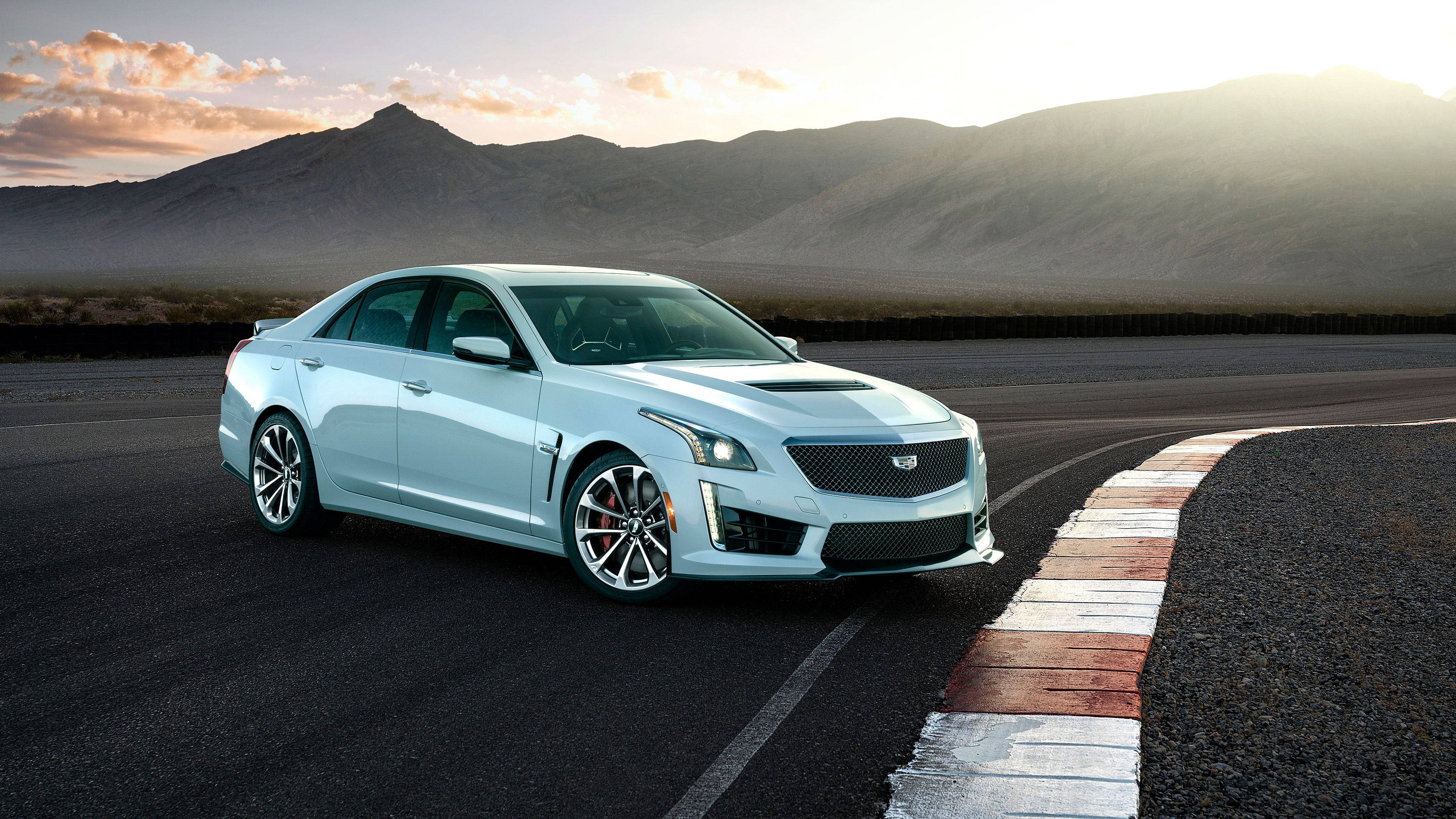 Cadillac 桌布 壁紙 — 一輛時尚的銀色Cadillac CTS-V在日落時分沿著沙漠賽道疾馳，背景是山脈。