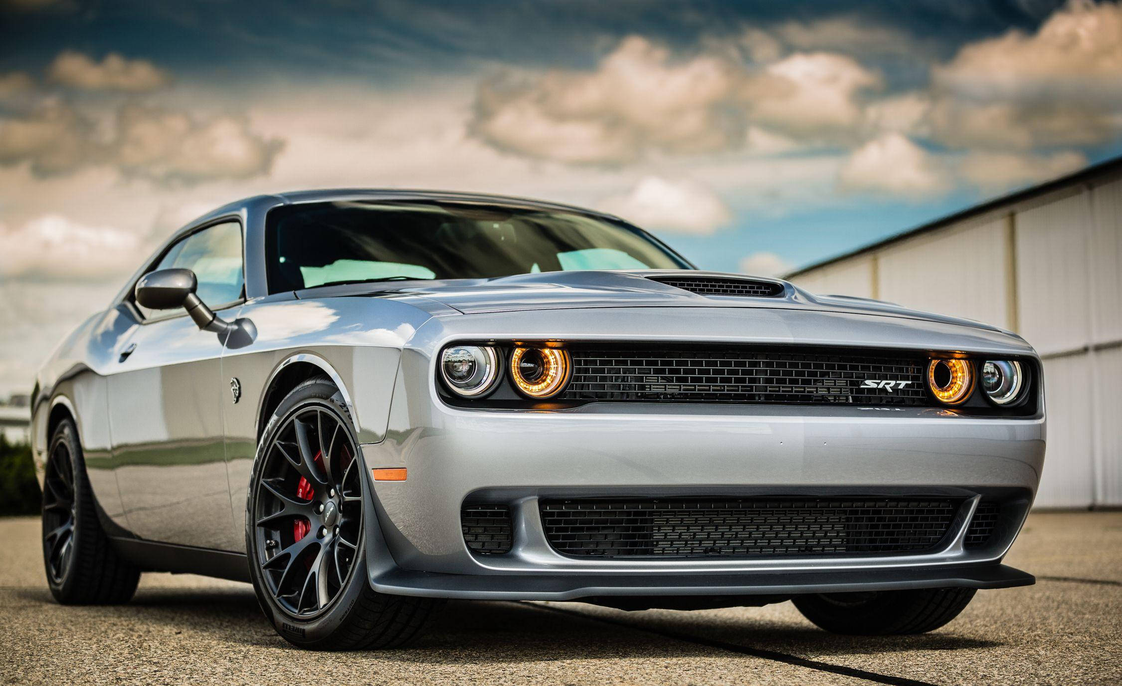Challenger 桌布 壁紙 — 一輛時尚的銀色Dodge Challenger SRT，帶有發光的橙色頭燈，停在陰天天空下的瀝青路面上。