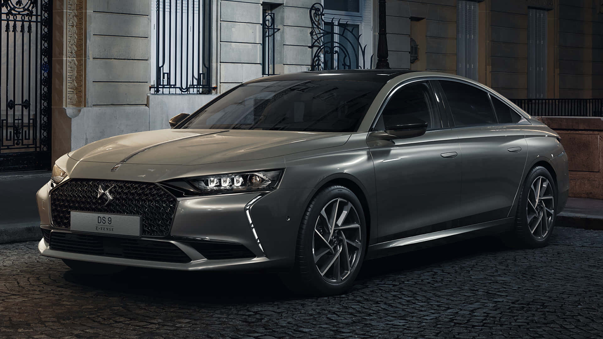 Ds Automobiles 桌布 壁紙 — 一輛時尚的銀色DS 9豪華轎車在夜晚停泊在鵝卵石街道上，背景是優雅的建築外牆。