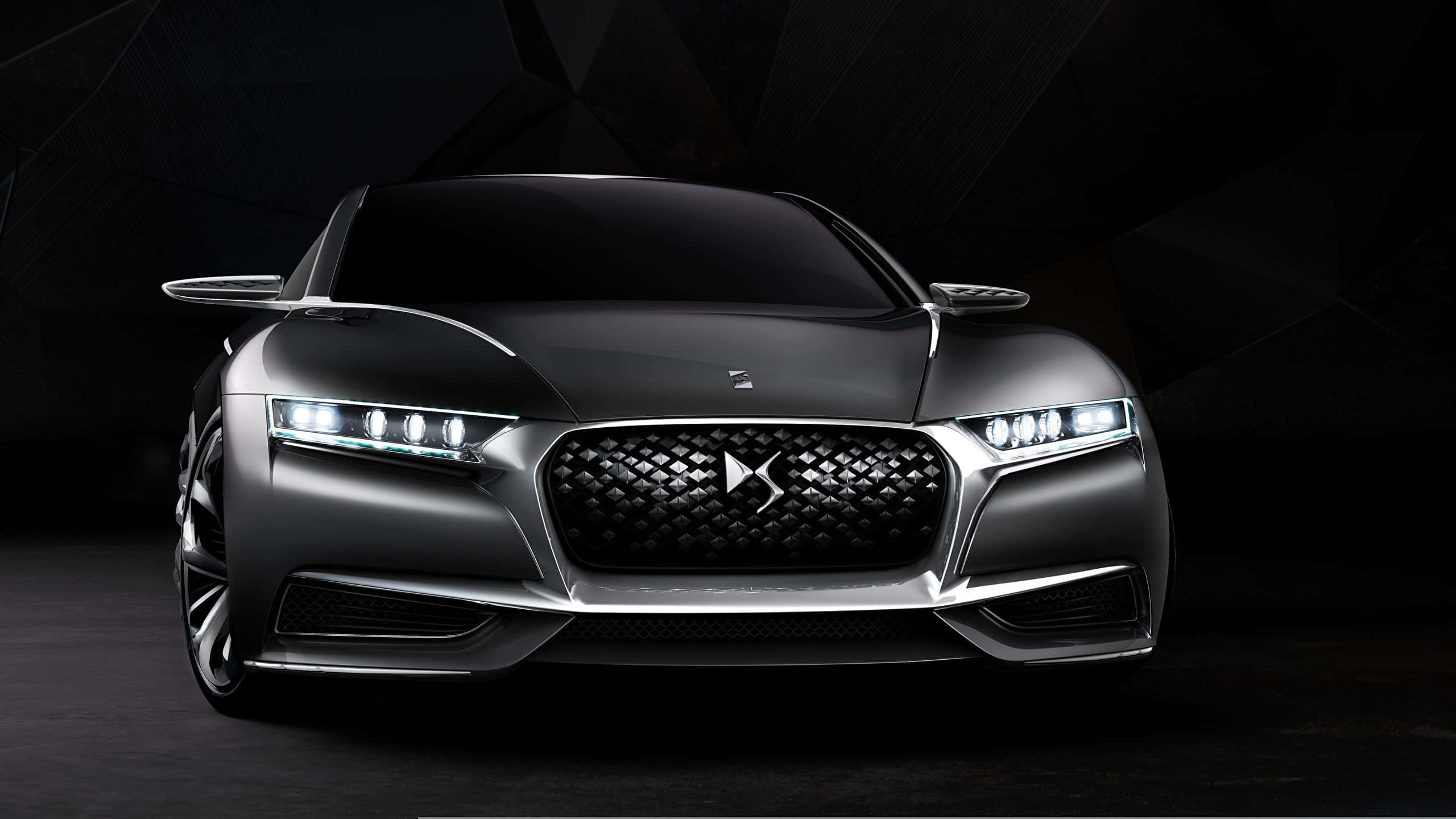 Ds Automobiles 桌布 壁紙 — 一輛時尚的銀色DS Automobiles概念車，配備發光頭燈和菱形圖案水箱護罩，在深色幾何工作室背景前展示。