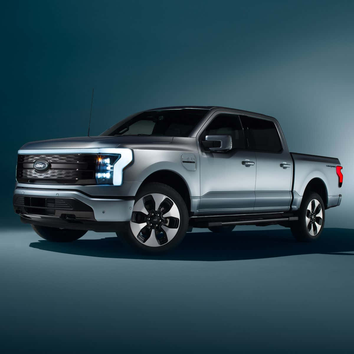 福特 桌布 壁紙 — 一輛時尚的銀色Ford F-150 Lightning皮卡車，配備發光頭燈和黑色輪圈，在漸變藍色工作室背景前展示。