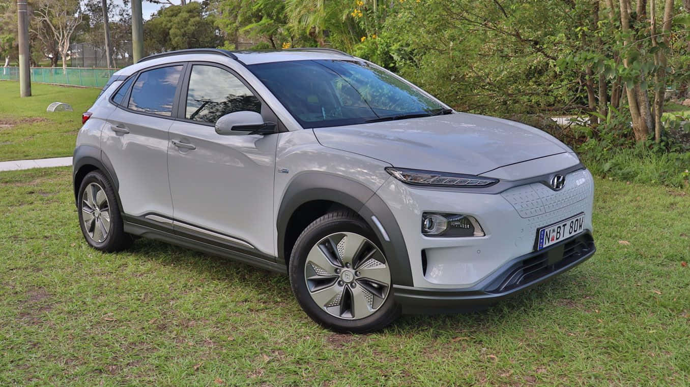 Electric Vehicle 桌布 壁紙 — 一輛時尚的銀色Hyundai Kona Electric SUV停放在草地上，背景有樹木和圍欄。