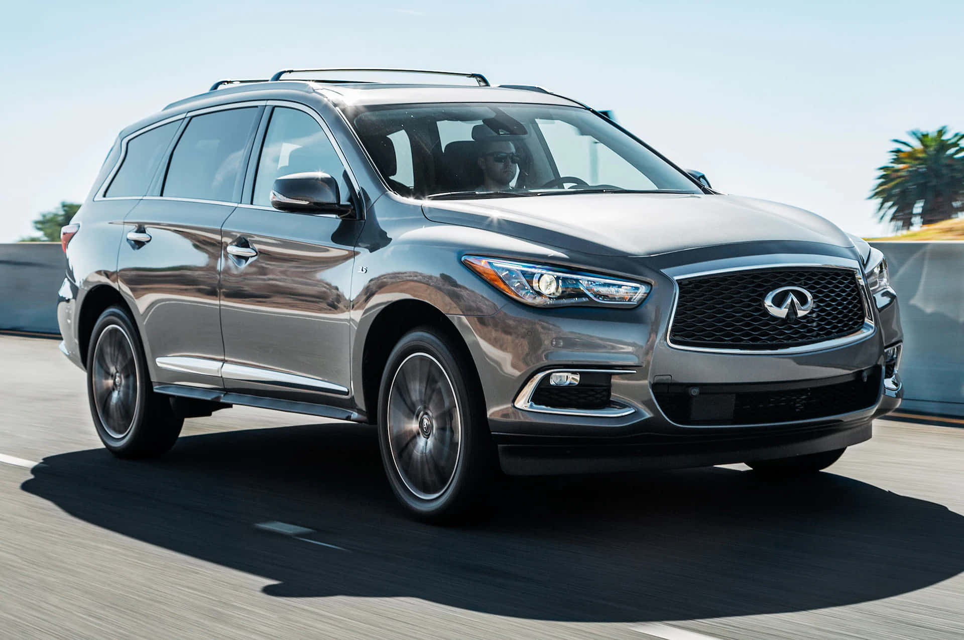 Infiniti Qx60 桌布 壁紙 — 一輛時尚的銀色Infiniti SUV在陽光明媚的高速公路上行駛，背景有棕櫚樹。