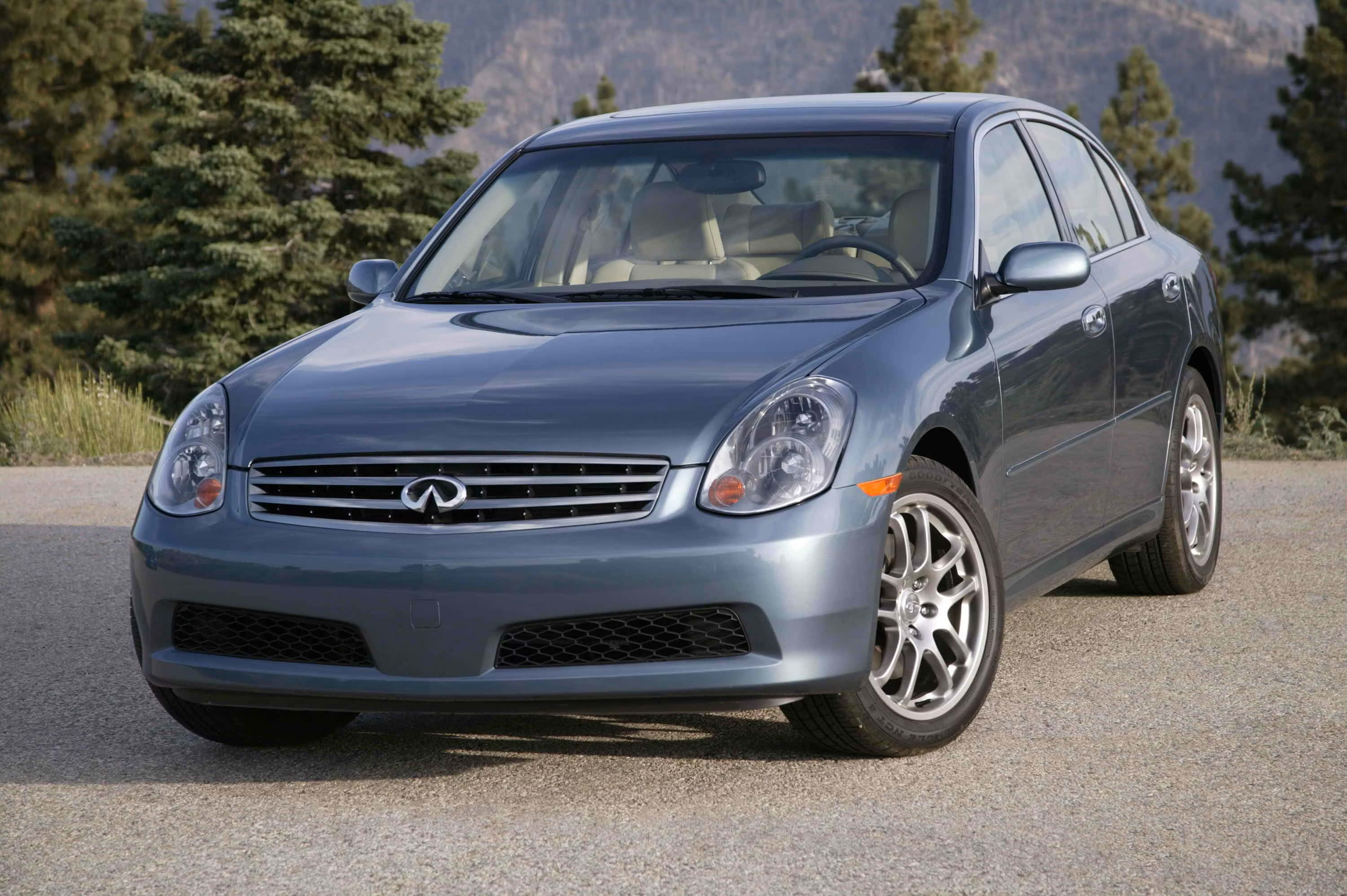 Infiniti G35 桌布 壁紙 — 一輛時尚的銀色Infiniti轎車停在碎石路上，背景有松樹和山脈。