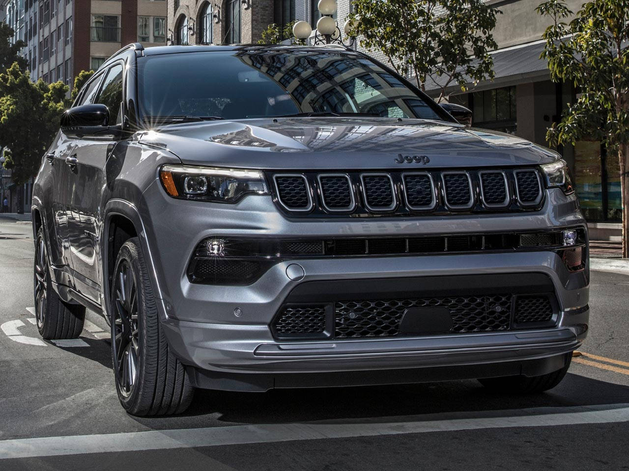 Road 桌布 壁紙 — 一輛時尚的銀色Jeep Grand Cherokee停放在陽光明媚的城市街道上，背景是現代建築和樹木。