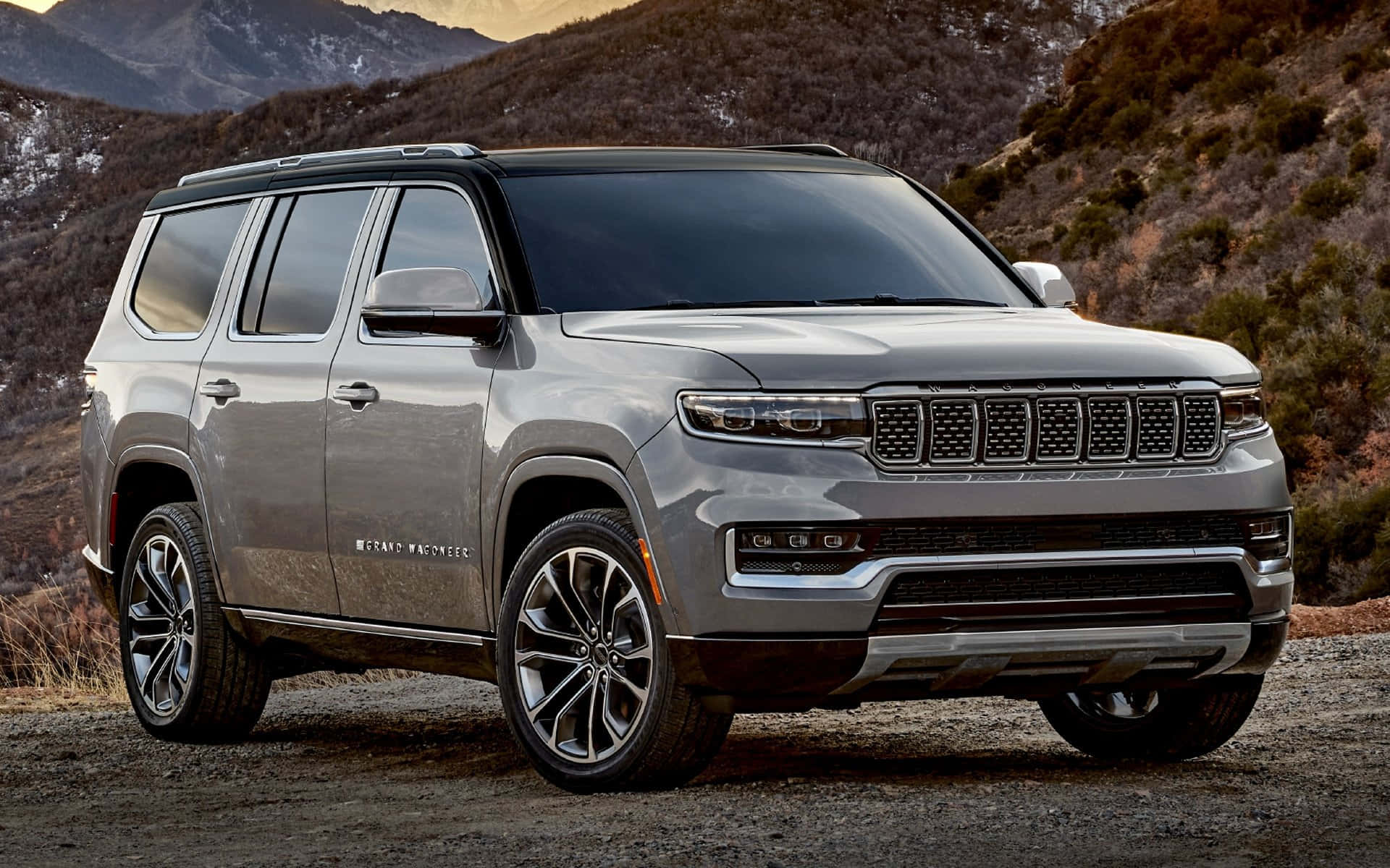 Jeep Wagoneer 桌布 壁紙 — 一輛時尚的銀色Jeep Grand Wagoneer SUV停在碎石路上，背景是崎嶇的山脈。