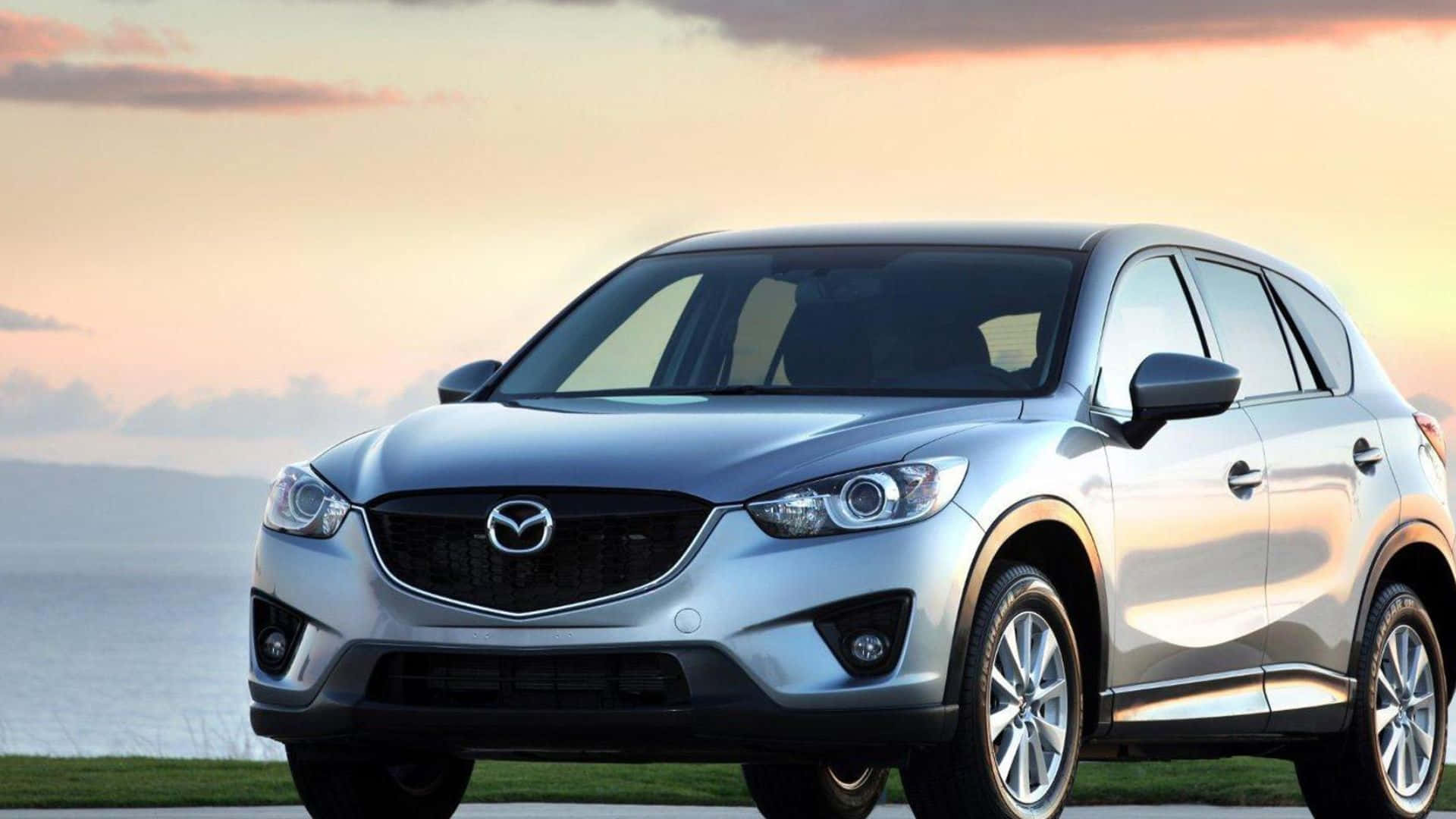 Mazda Cx-5 桌布 壁紙 — 一輛時尚的銀色Mazda CX-5 SUV停泊在日落時分的海邊，溫暖的金色光線在其拋光表面上反射。