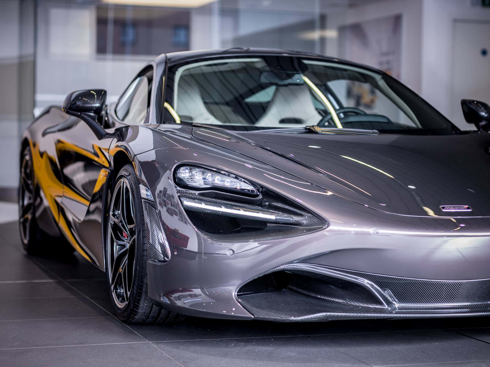 麥拉倫 720S 桌布 壁紙 — 一輛時尚的銀色McLaren 720S，帶有醒目的黃色點綴，在明亮的展廳燈光下閃閃發光。