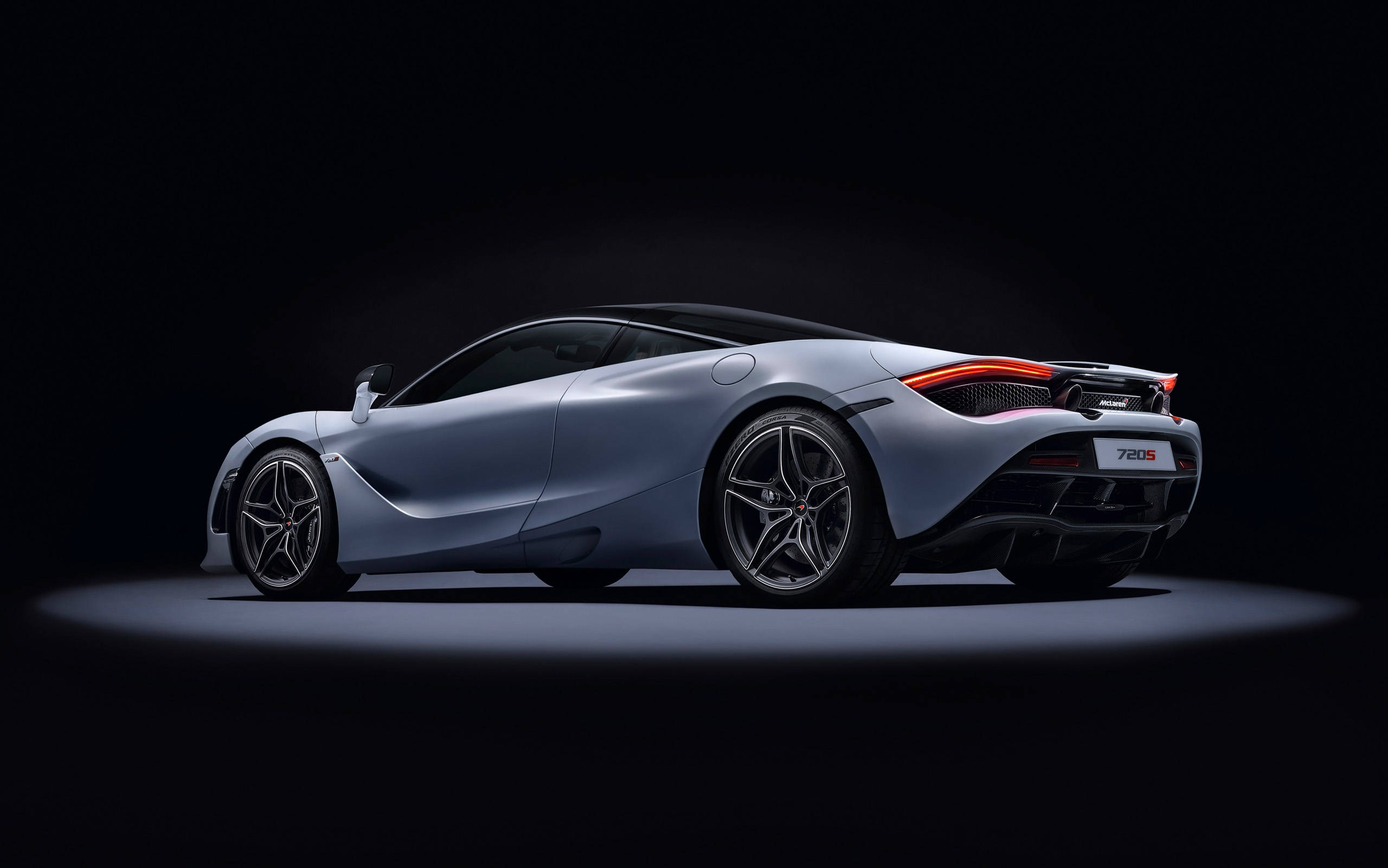mclaren 720s 4K 桌布 壁紙 — 一輛時尚的銀色McLaren 720S跑車在黑色工作室背景下，在聚光燈下閃耀，紅色尾燈亮起。