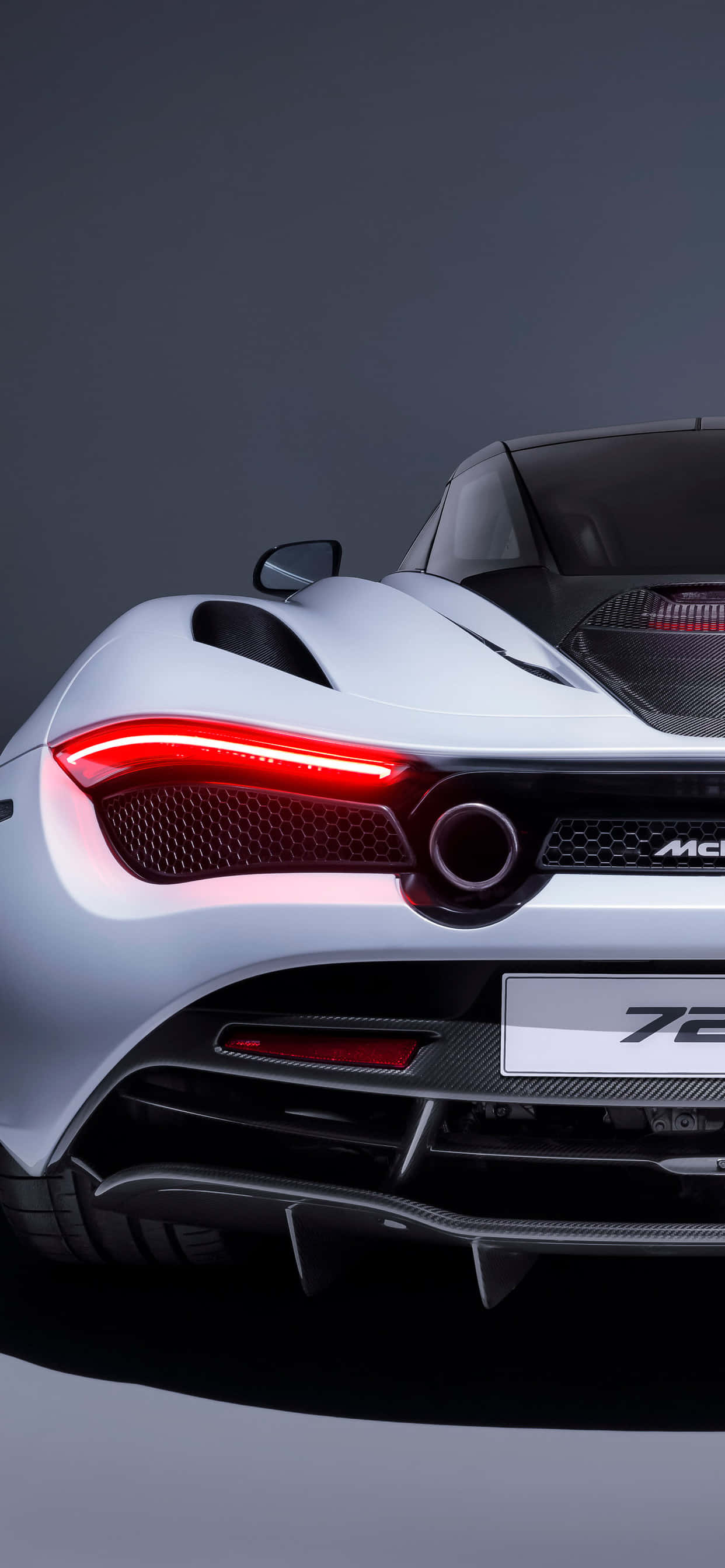 電玩遊戲 桌布 壁紙 — 一輛時尚的銀色McLaren 720S跑車後視圖，帶有發光的紅色尾燈，背景為深色工作室。