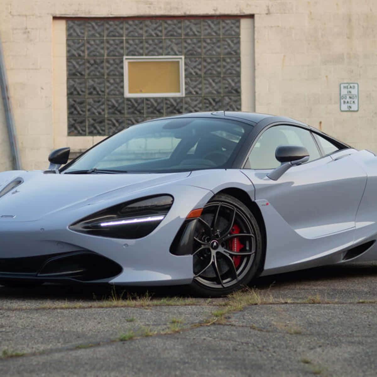 Gray Aesthetic 桌布 壁紙 — 一輛時尚的銀色McLaren 720S跑車停在裂開的柏油路上，前方是一座帶有圖案玻璃窗的風化工業建築。