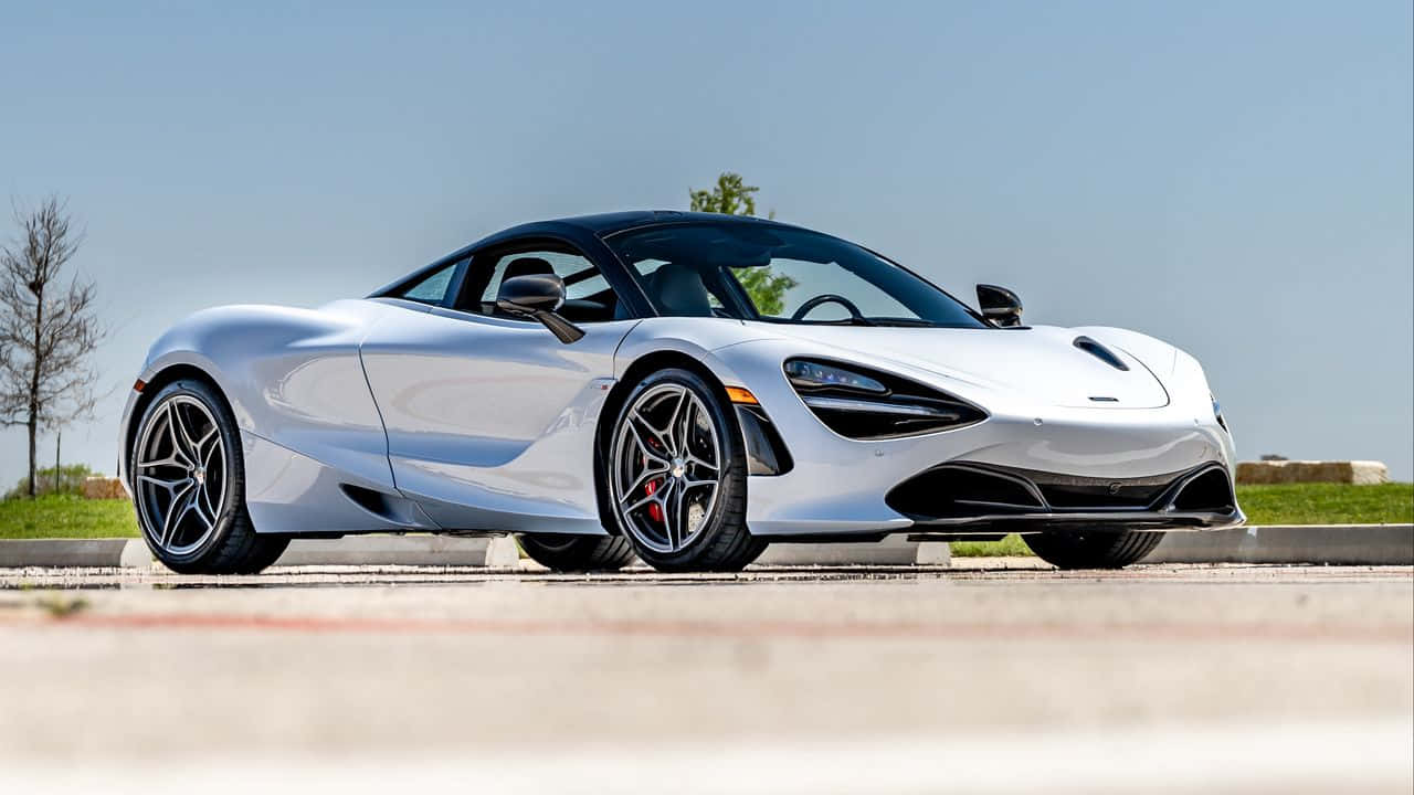 汽車 桌布 壁紙 — 一輛時尚的銀色McLaren 720S跑車停放在鋪砌的地面上，周圍有草地和樹木，天空湛藍清澈。