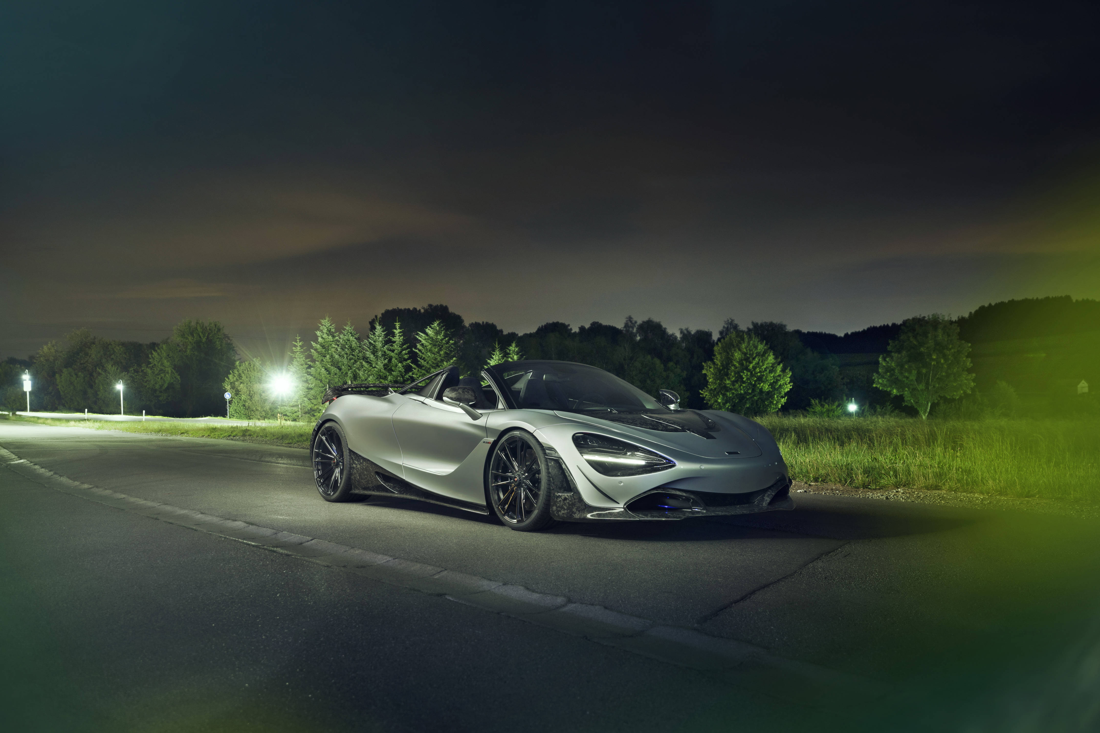 Mclaren 720s 桌布 壁紙 — 一輛時尚的銀色McLaren Speedtail敞篷車在寧靜的鄉村道路上，樹木環繞，在夜燈下閃閃發光。