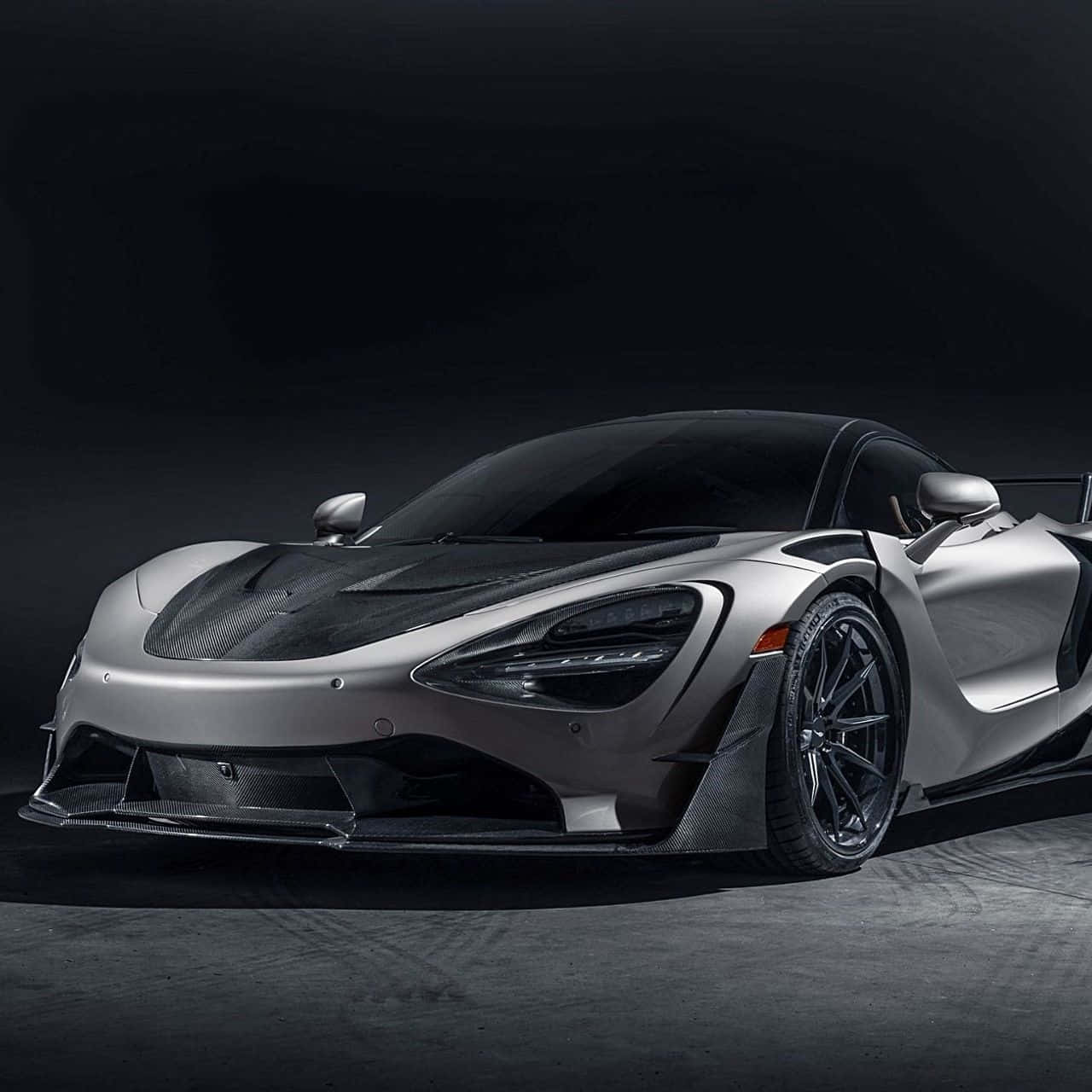 麥拉倫 桌布 壁紙 — 一輛時尚的銀色McLaren Senna超級跑車帶有碳纖維裝飾，在黑暗的攝影棚背景下戲劇性地照亮。