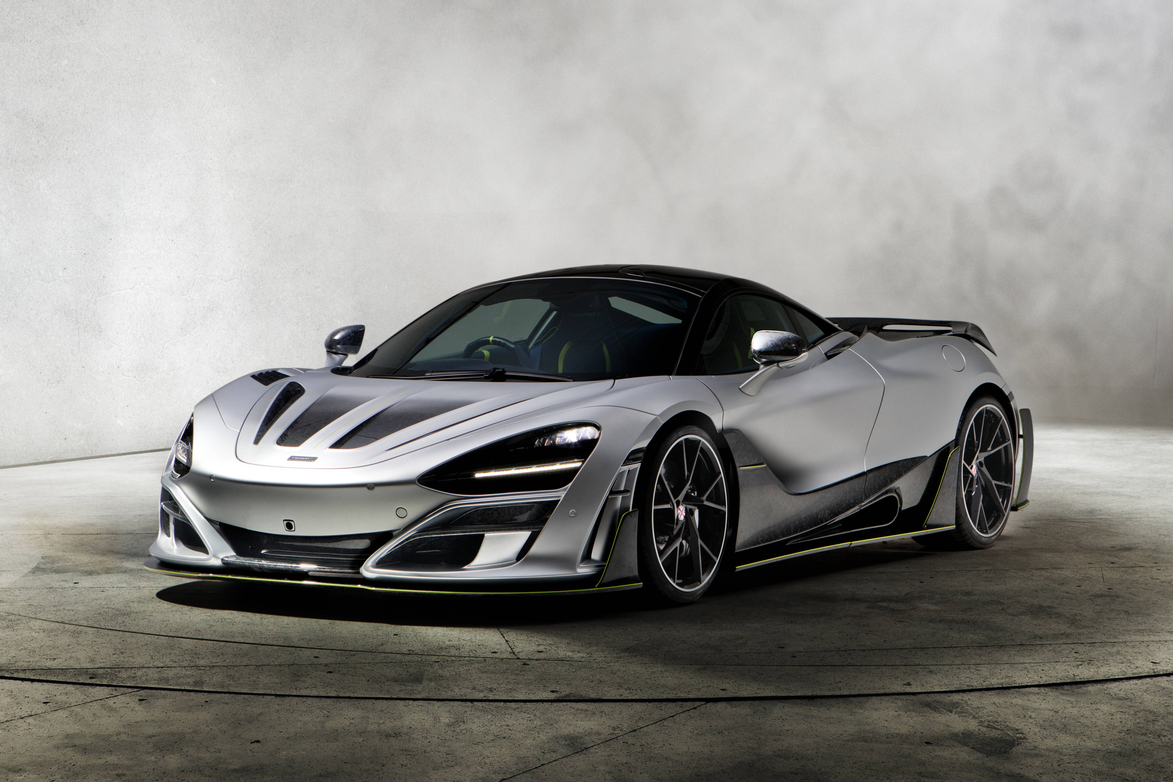 Mclaren 720s 桌布 壁紙 — 一輛時尚的銀色McLaren超級跑車，帶有黑色飾邊和黃色裝飾，在一個極簡主義的工作室中展示，地板是混凝土的，牆壁有紋理。