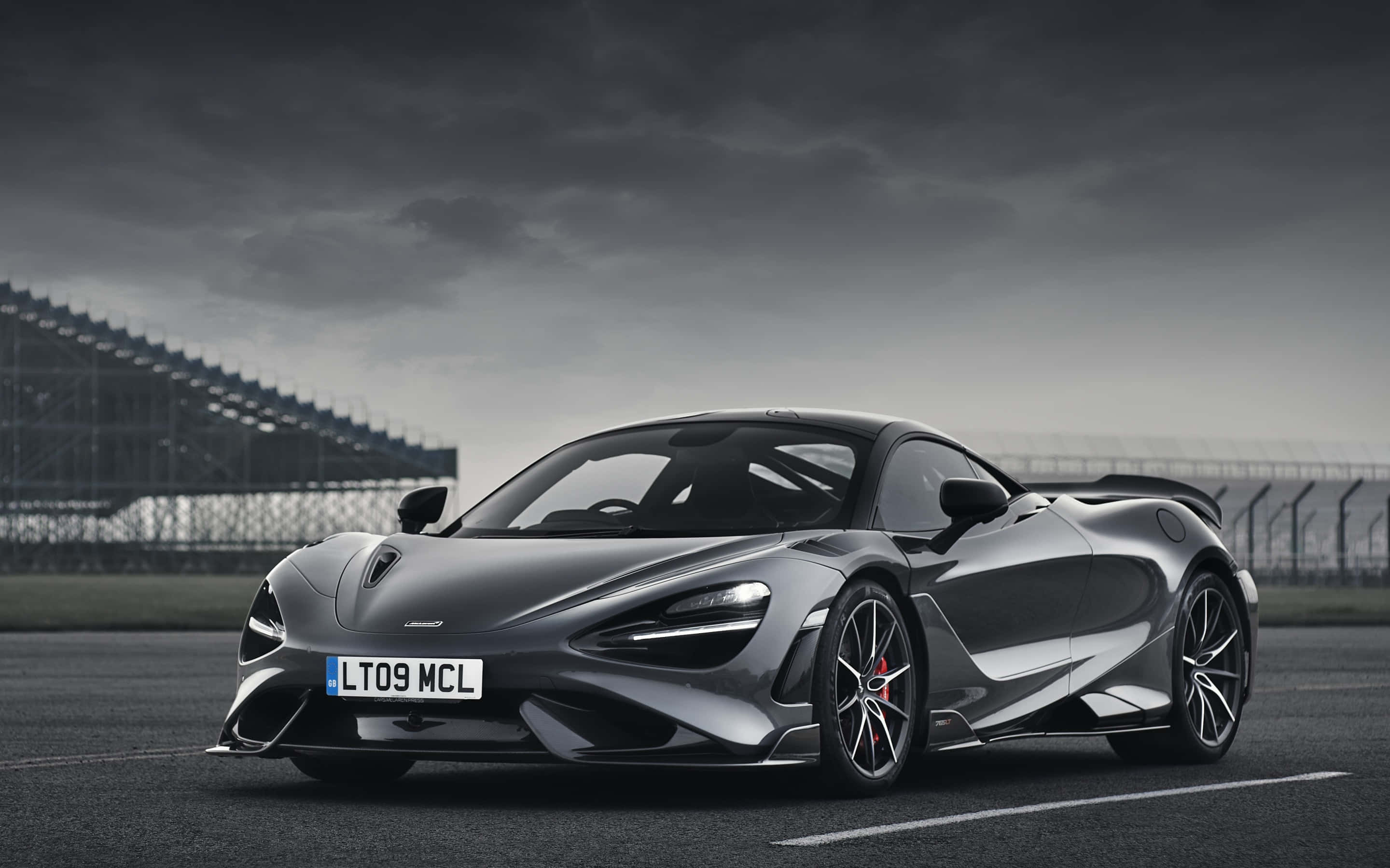 麥拉倫 桌布 壁紙 — 一輛時尚的銀色McLaren跑車停在賽道上，背景是陰沉多雲的天空和看台。