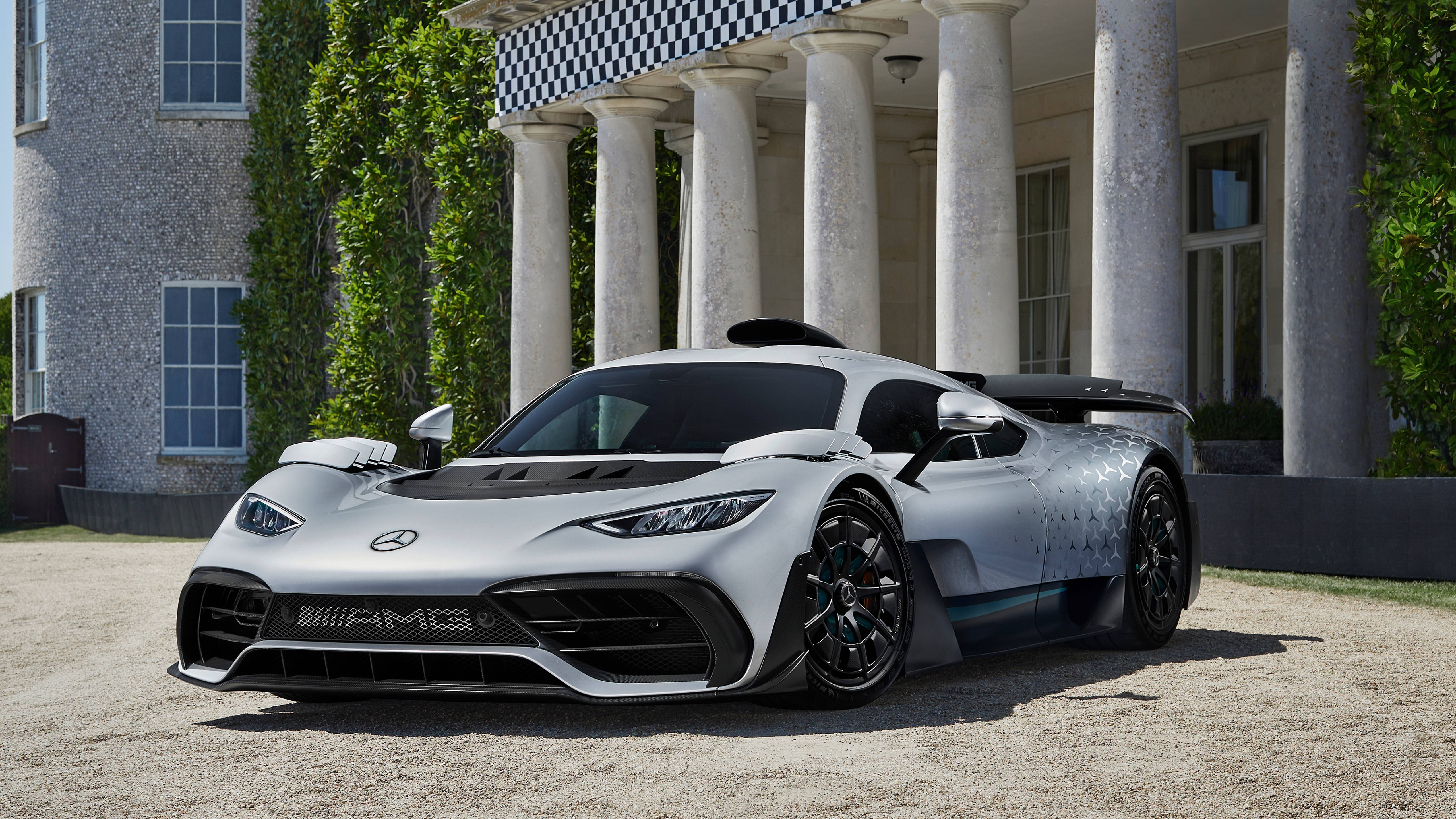 Mercedes 桌布 壁紙 — 一輛時尚的銀色Mercedes-AMG One hypercar停泊在碎石路上，前方是一座有柱廊和常春藤覆蓋牆壁的宏偉大宅。