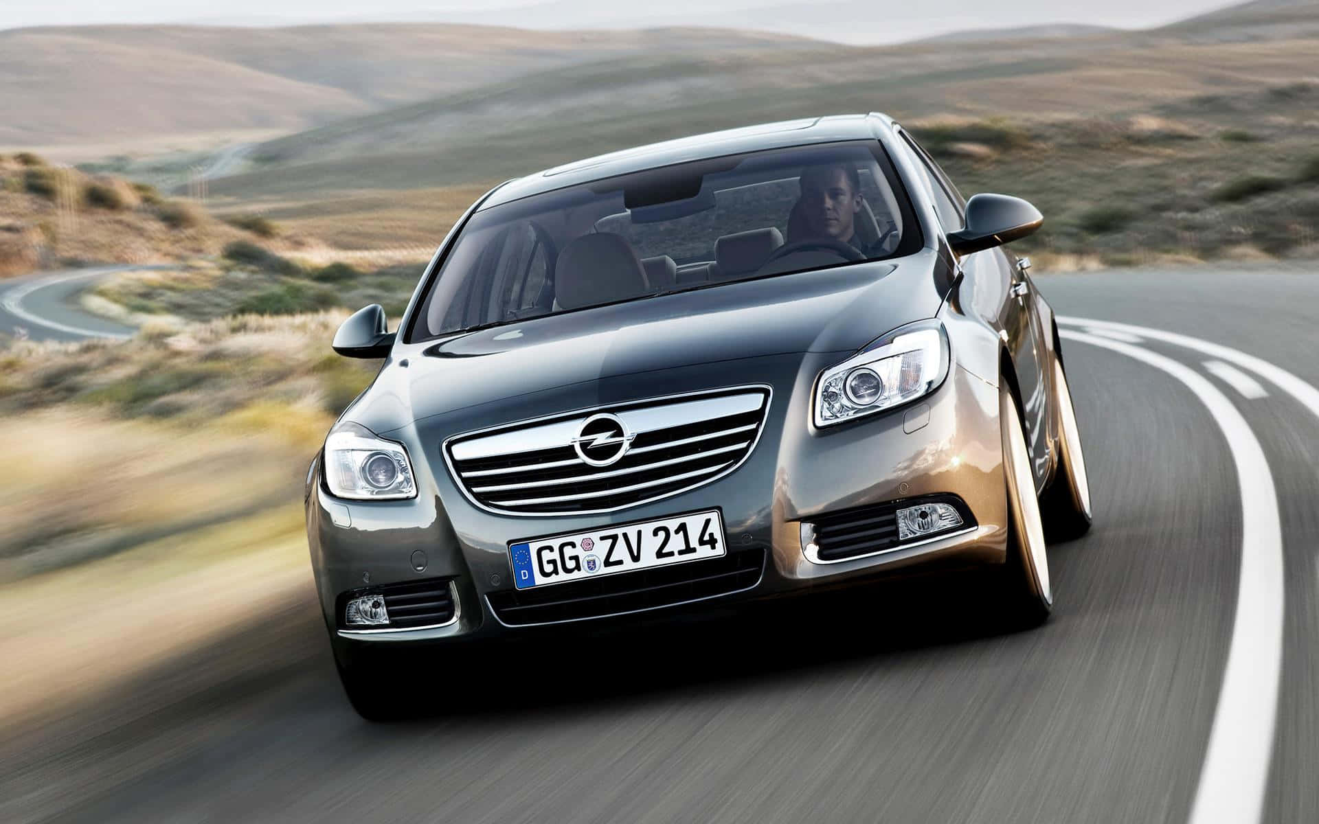 Opel Insignia 桌布 壁紙 — 一輛時尚的銀色Opel Insignia在蜿蜒的山路上疾馳，風景模糊。