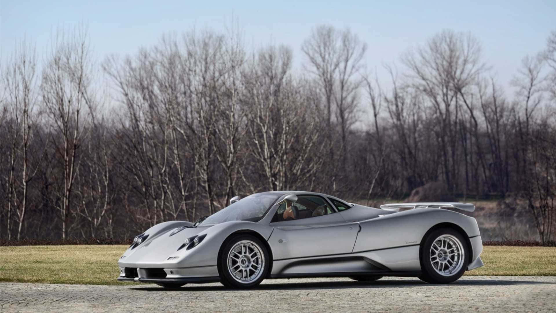 Pagani Zonda C12 Roadster 桌布 壁紙 — 一輛時尚的銀色Pagani超級跑車停在鵝卵石路上，背景是光禿禿的樹木，天空晴朗。