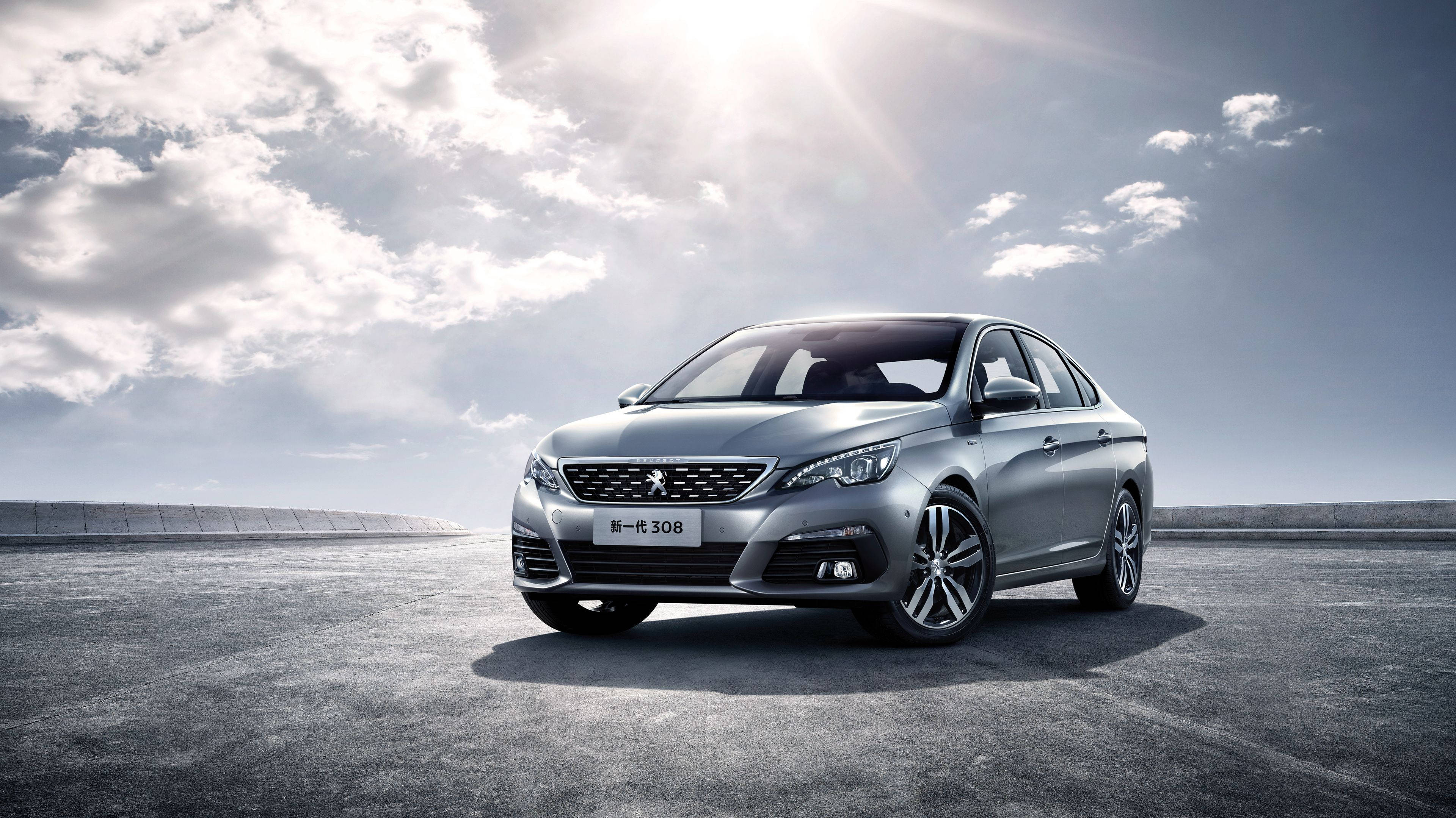 Peugeot 桌布 壁紙 — 一輛時尚的銀色Peugeot 308轎車在明亮的陽光下，以戲劇性的多雲天空為背景，在廣闊的混凝土路面上閃閃發光。