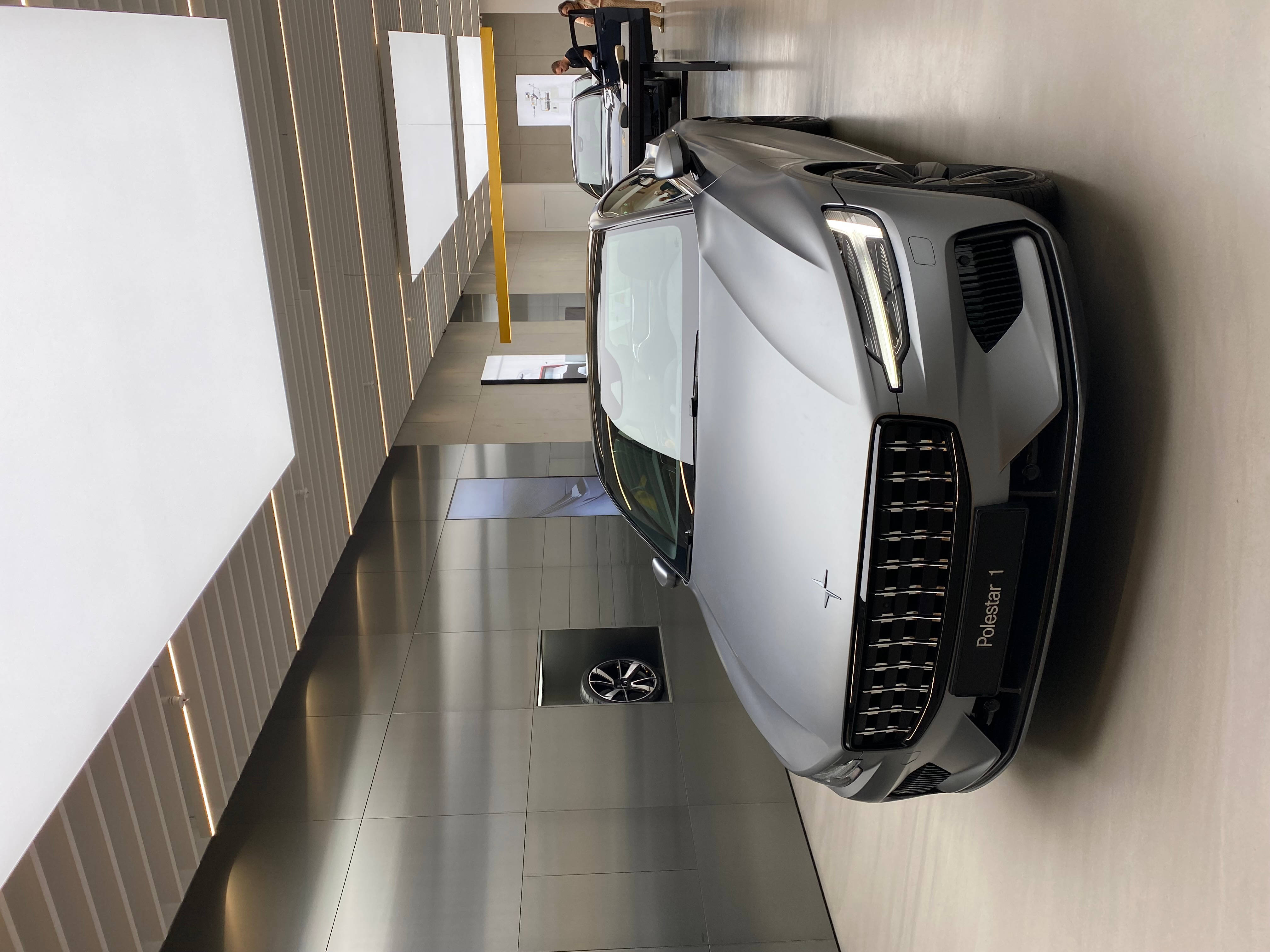 高清汽車 桌布 壁紙 — 一輛時尚的銀色Polestar 1跑車垂直安裝在現代簡約展廳的淺色木牆上。