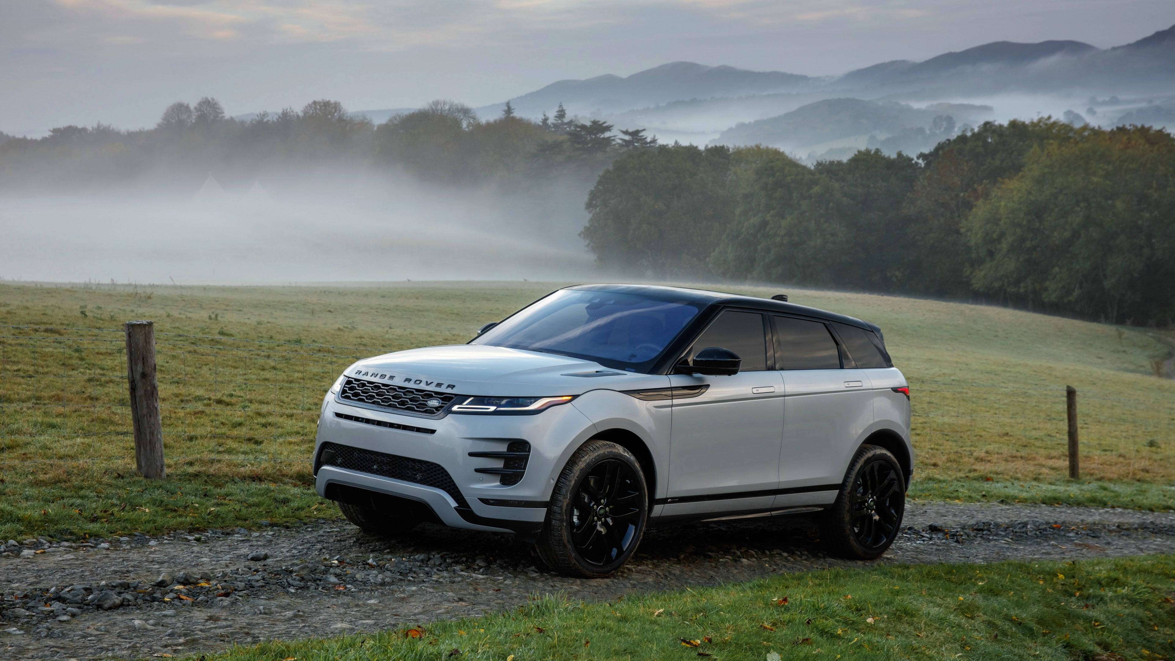 高清 桌布 壁紙 — 一輛時尚的銀色Range Rover Evoque停泊在霧氣瀰漫的碎石路上，背景是起伏的綠色山丘和霧濛濛的森林。