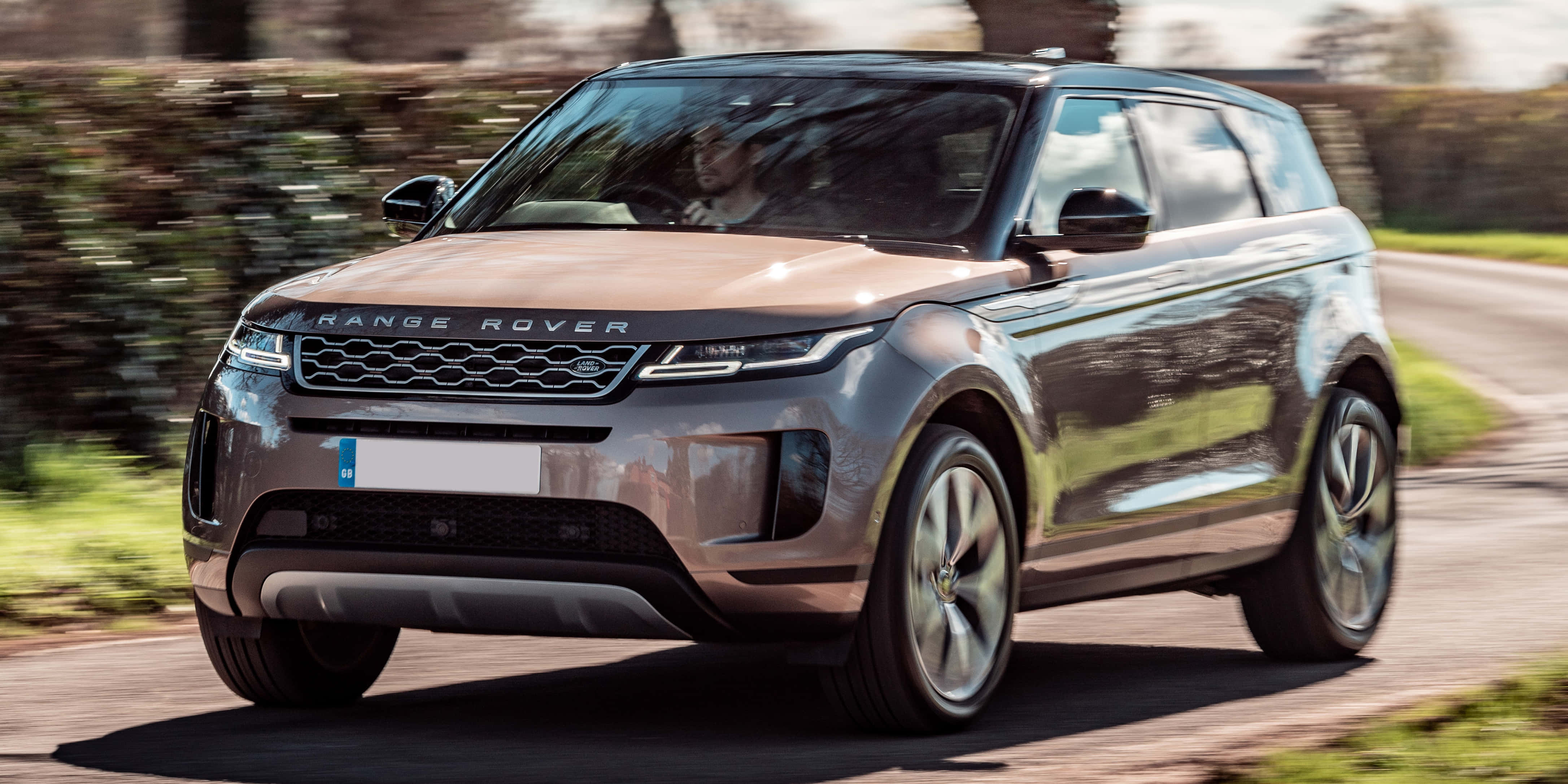 Range Rover 桌布 壁紙 — 一輛時尚的銀色Range Rover Evoque在陽光明媚的鄉村道路上疾馳，背景的綠色植物呈現動態模糊。