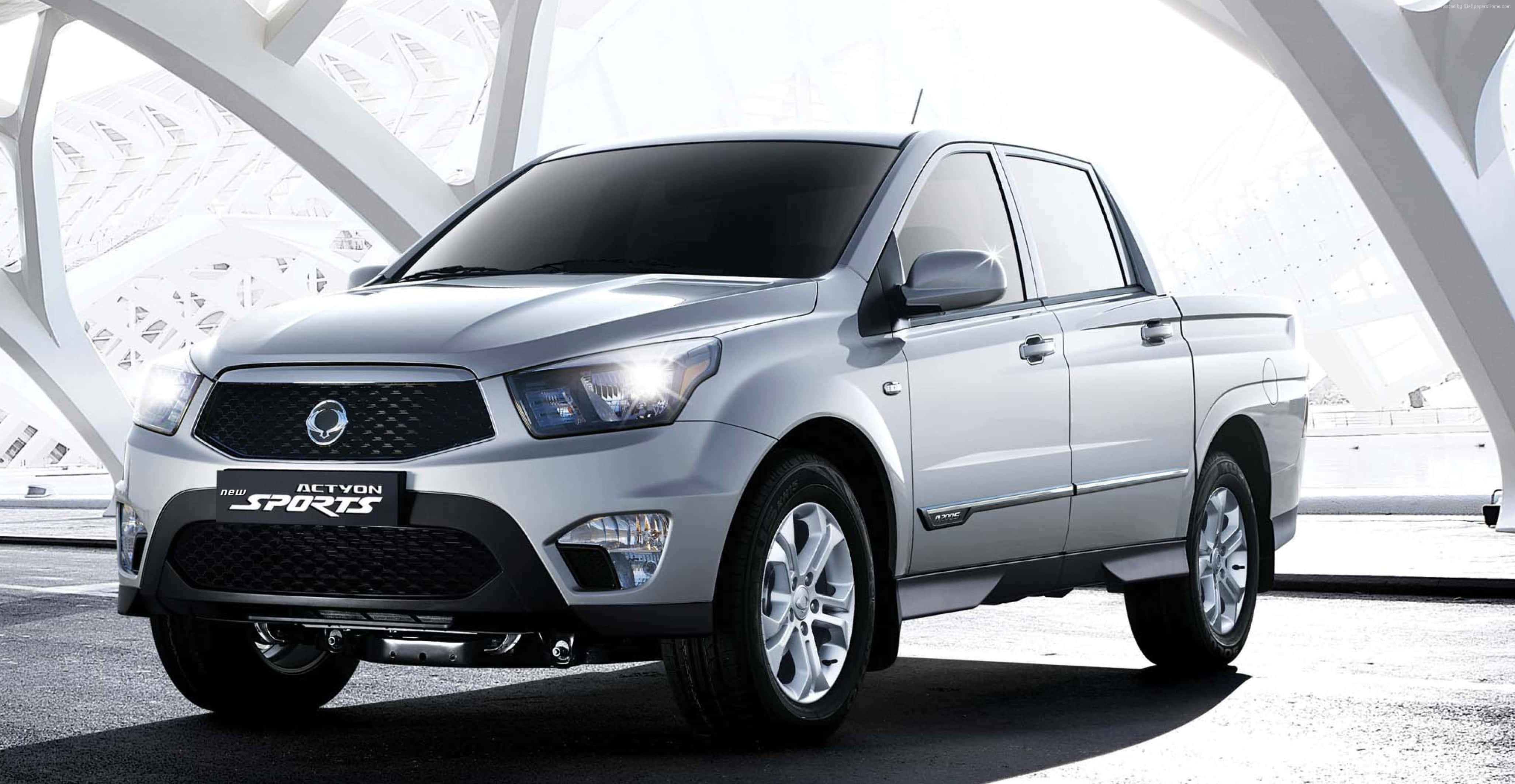 Ssangyong 桌布 壁紙 — 一輛時尚的銀色SsangYong Actyon Sports皮卡車在明亮的日光下，於現代白色建築結構下展示。