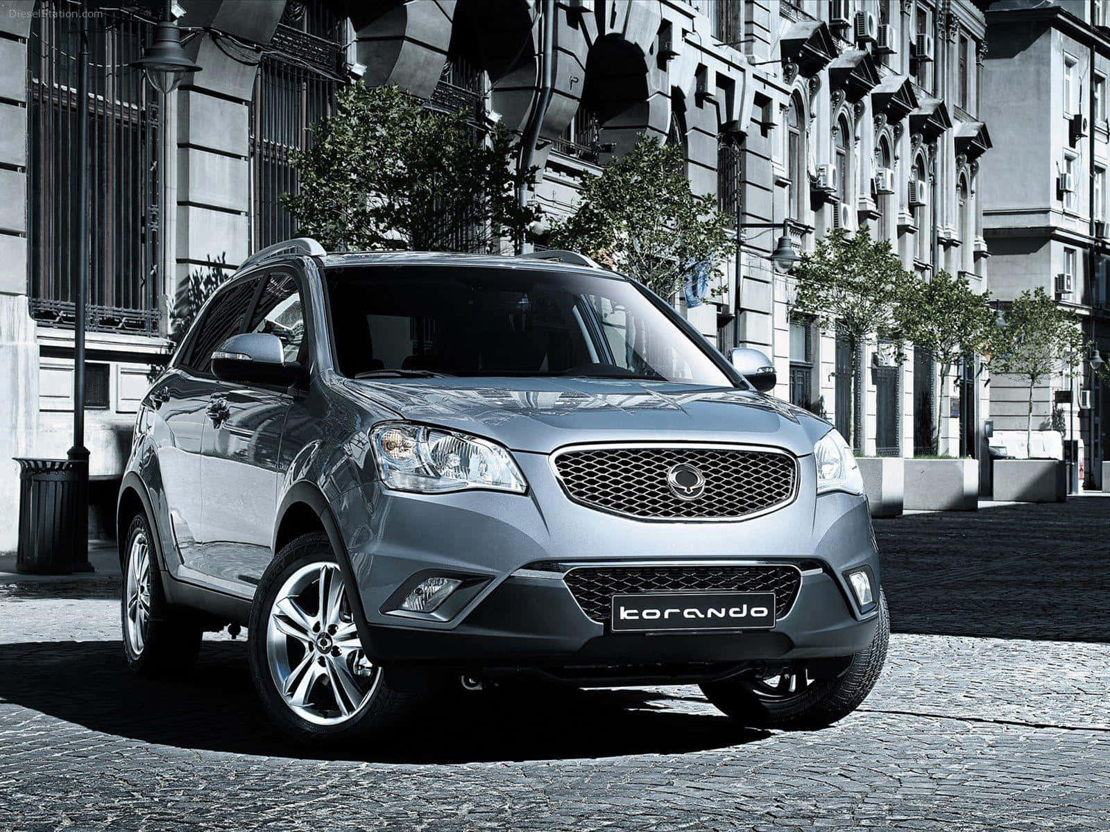 Ssangyong 桌布 壁紙 — 一輛時尚的銀色SsangYong Korando SUV停泊在鵝卵石街道上，前方是華麗的歐式建築。