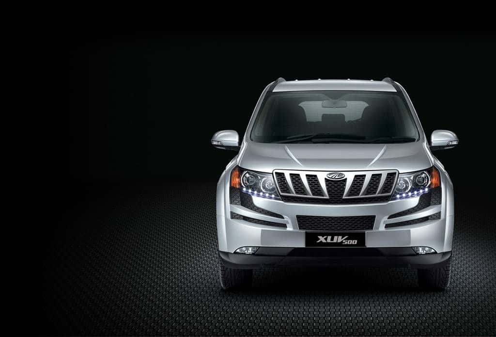Mahindra 桌布 壁紙 — 一輛時尚的銀色SUV，帶有發光的頭燈，居中站立在深色紋理地板上，背景為黑色。
