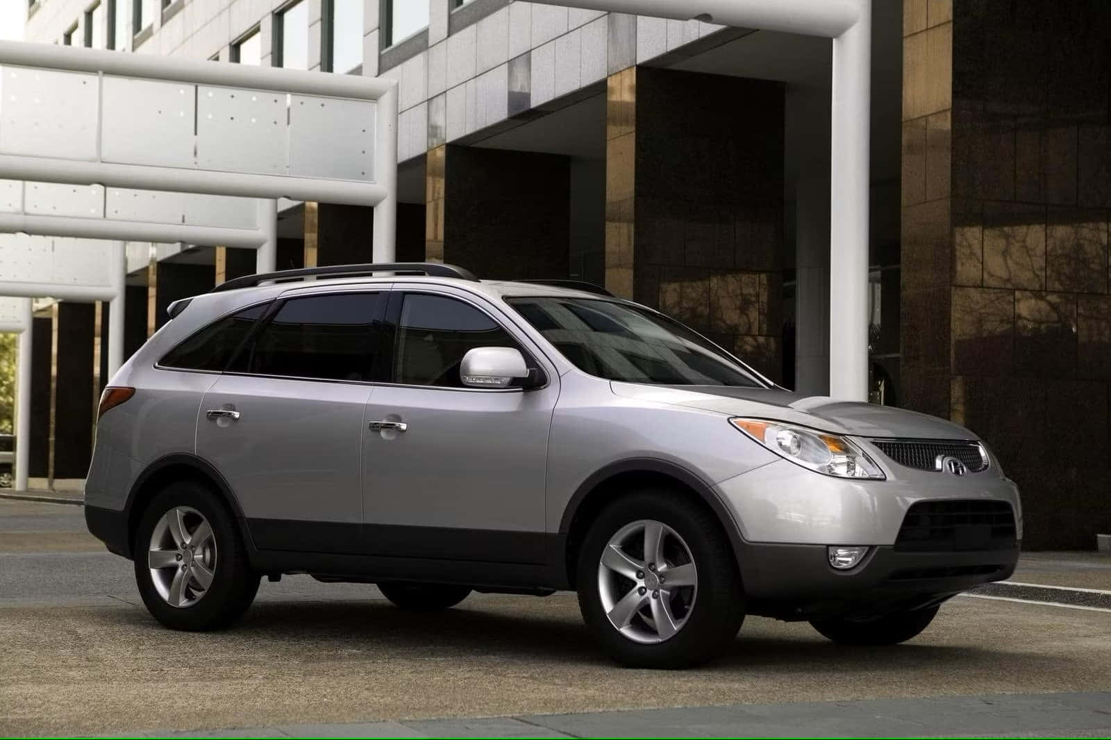Hyundai Veracruz 桌布 壁紙 — 一輛時尚的銀色SUV停在一棟現代玻璃和鋼結構建築前，建築有白色柱子。