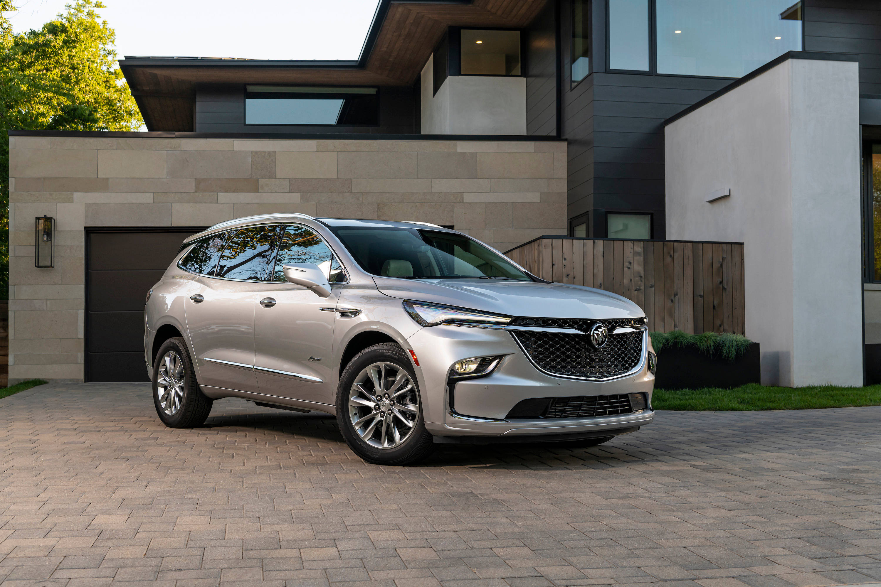 Buick 桌布 壁紙 — 一輛時尚的銀色SUV停在磚砌車道上，前面是一座採用石材和玻璃建築風格的現代房屋。
