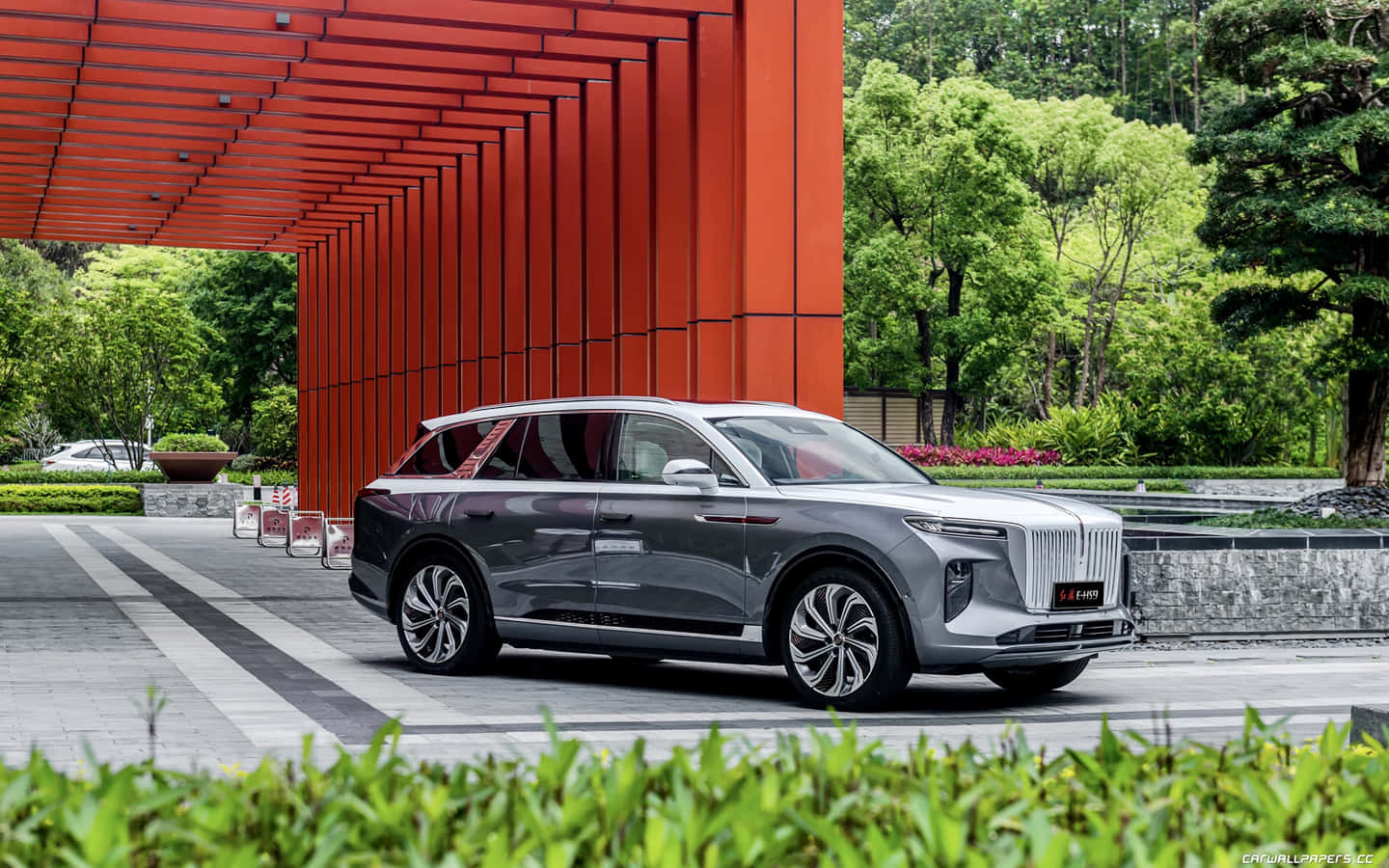 Hongqi 桌布 壁紙 — 一輛時尚的銀色SUV停放在大膽的紅色幾何天篷下，周圍環繞著茂密的綠植，營造出現代都市氛圍。