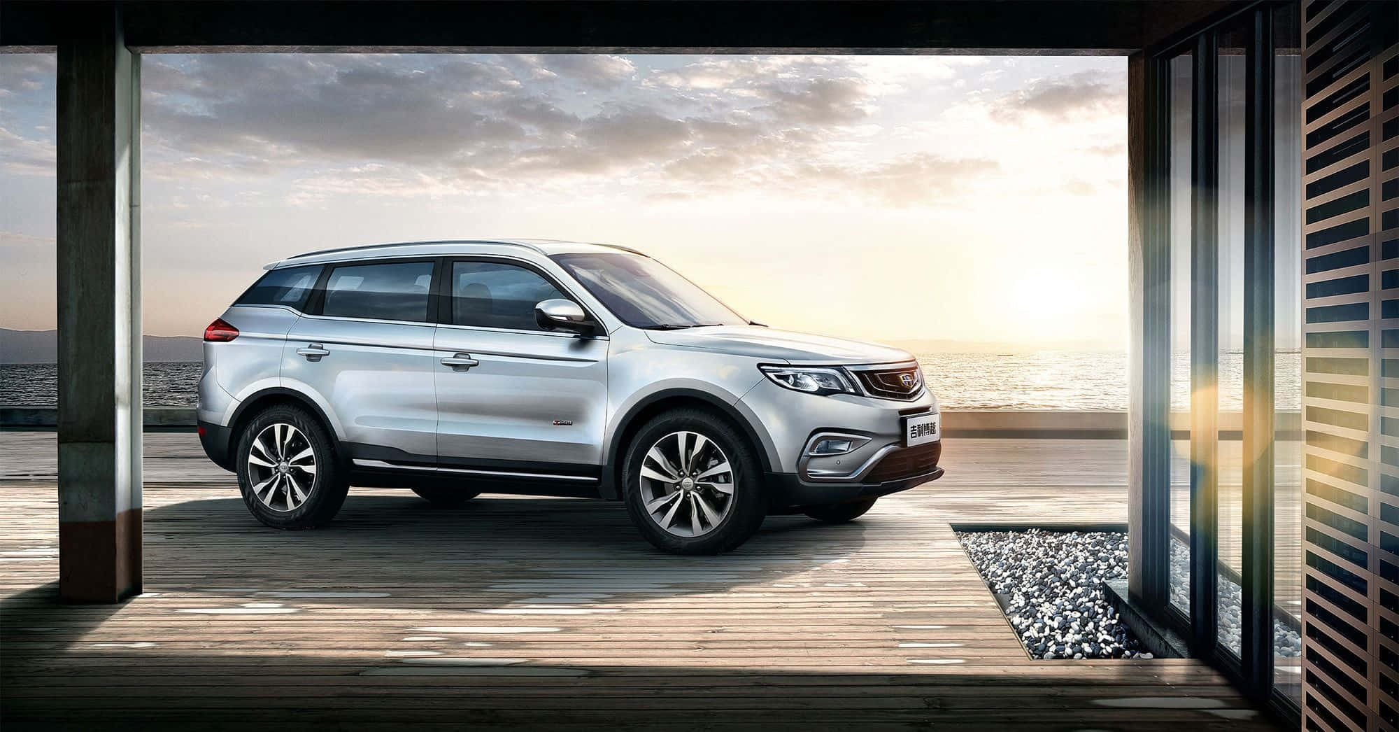 Geely 桌布 壁紙 — 一輛時尚的銀色SUV停放在木製甲板上，透過玻璃門欣賞日落時分的海景。