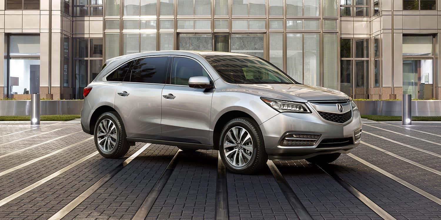 Acura Mdx 桌布 壁紙 — 一輛時尚的銀色SUV停放在現代磚砌廣場上，前方是玻璃幕牆的都市建築。