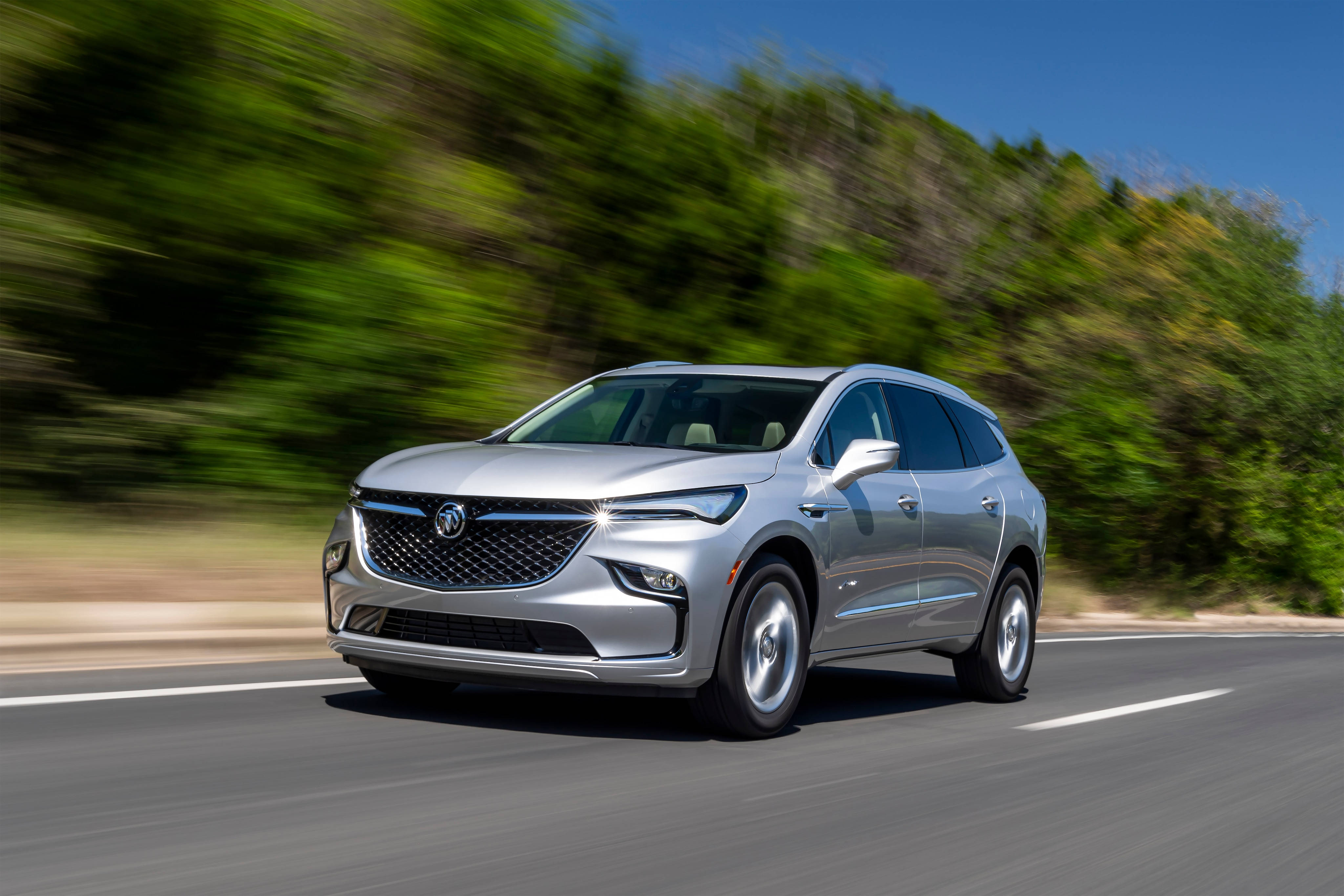 Buick 桌布 壁紙 — 一輛時尚的銀色SUV在陽光明媚的道路上行駛，茂密的綠樹在運動中模糊掠過。