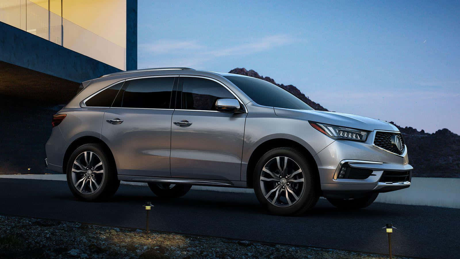 Acura Mdx 桌布 壁紙 — 一輛時尚的銀色SUV在黃昏時停泊在現代化車道上，背景是山脈。