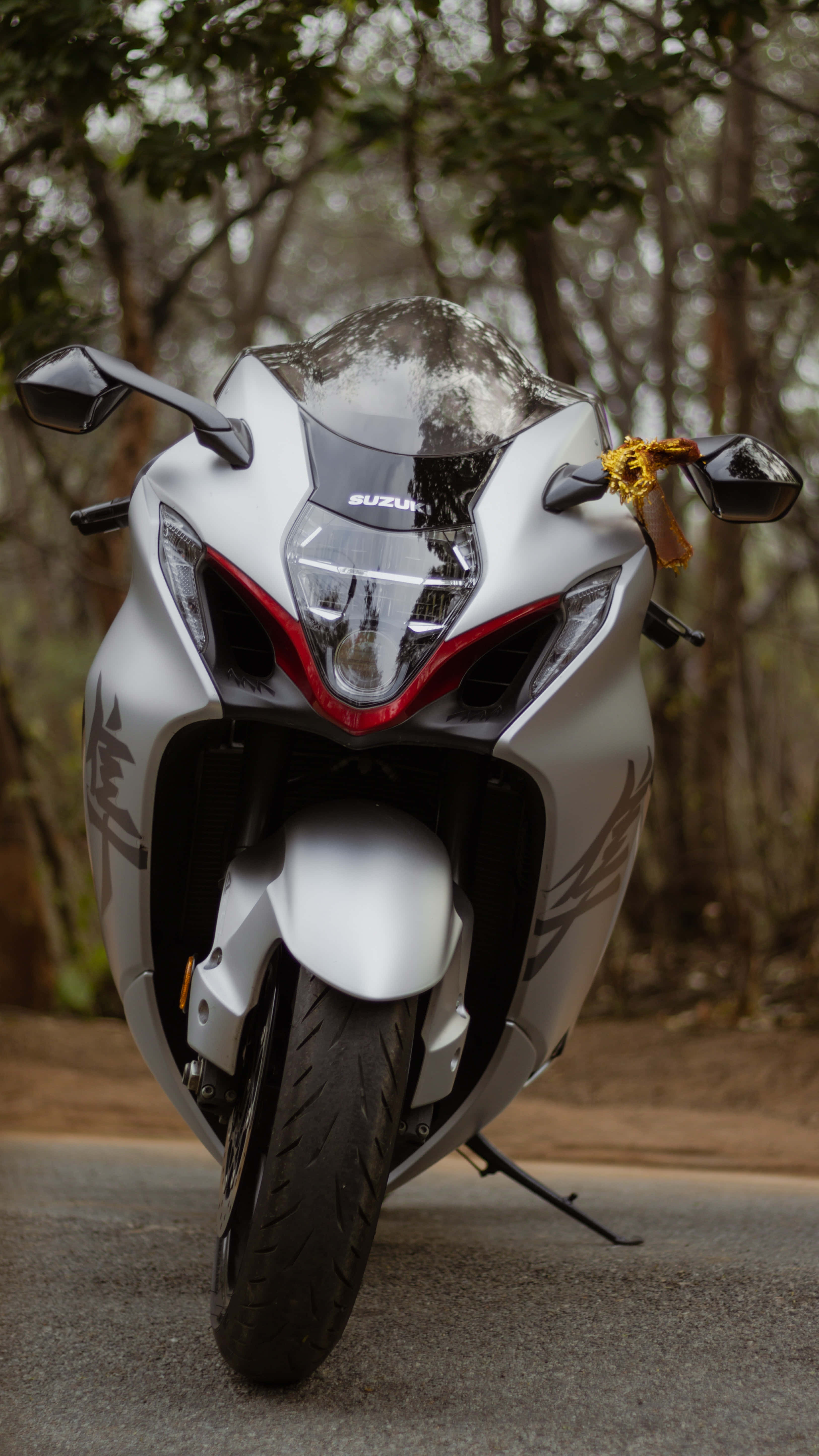 Superbike 桌布 壁紙 — 一輛時尚的銀色Suzuki機車，帶有紅色點綴和金色絲帶，停在森林道路上。