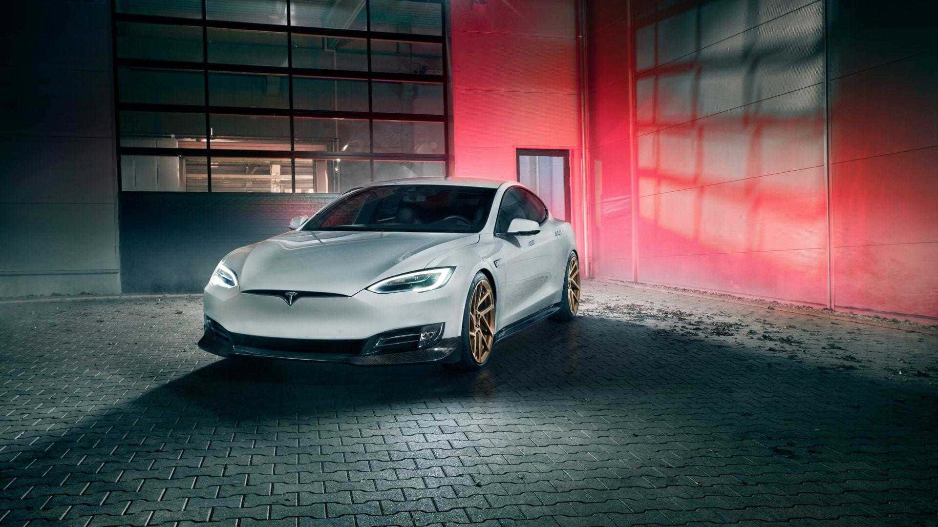 特斯拉 桌布 壁紙 — 一輛時尚的銀色Tesla Model S配金色輪圈，停在鵝卵石地面上，上方有戲劇性的紅色牆壁照明。