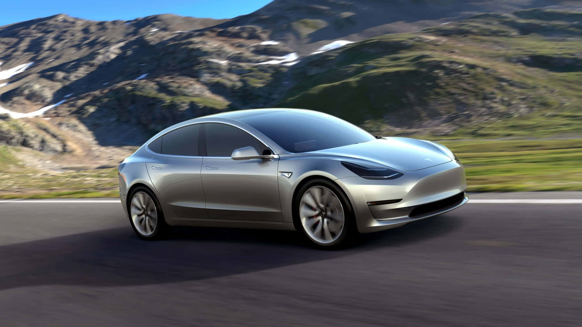 Tesla Model 3 桌布 壁紙 — 一輛時尚的銀色Tesla Model 3在蜿蜒的山路上行駛，周圍是白雪覆蓋的山峰和翠綠的山坡，天空湛藍清澈。
