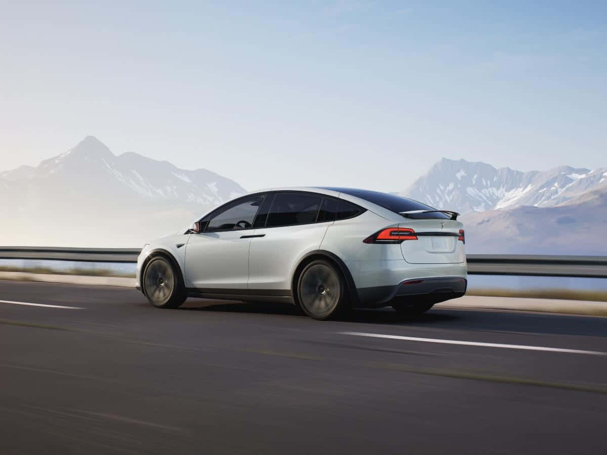 特斯拉 桌布 壁紙 — 一輛時尚的銀色Tesla Model X在高速公路上行駛，遠處朦朧的雪山在晴朗的天空下聳立。
