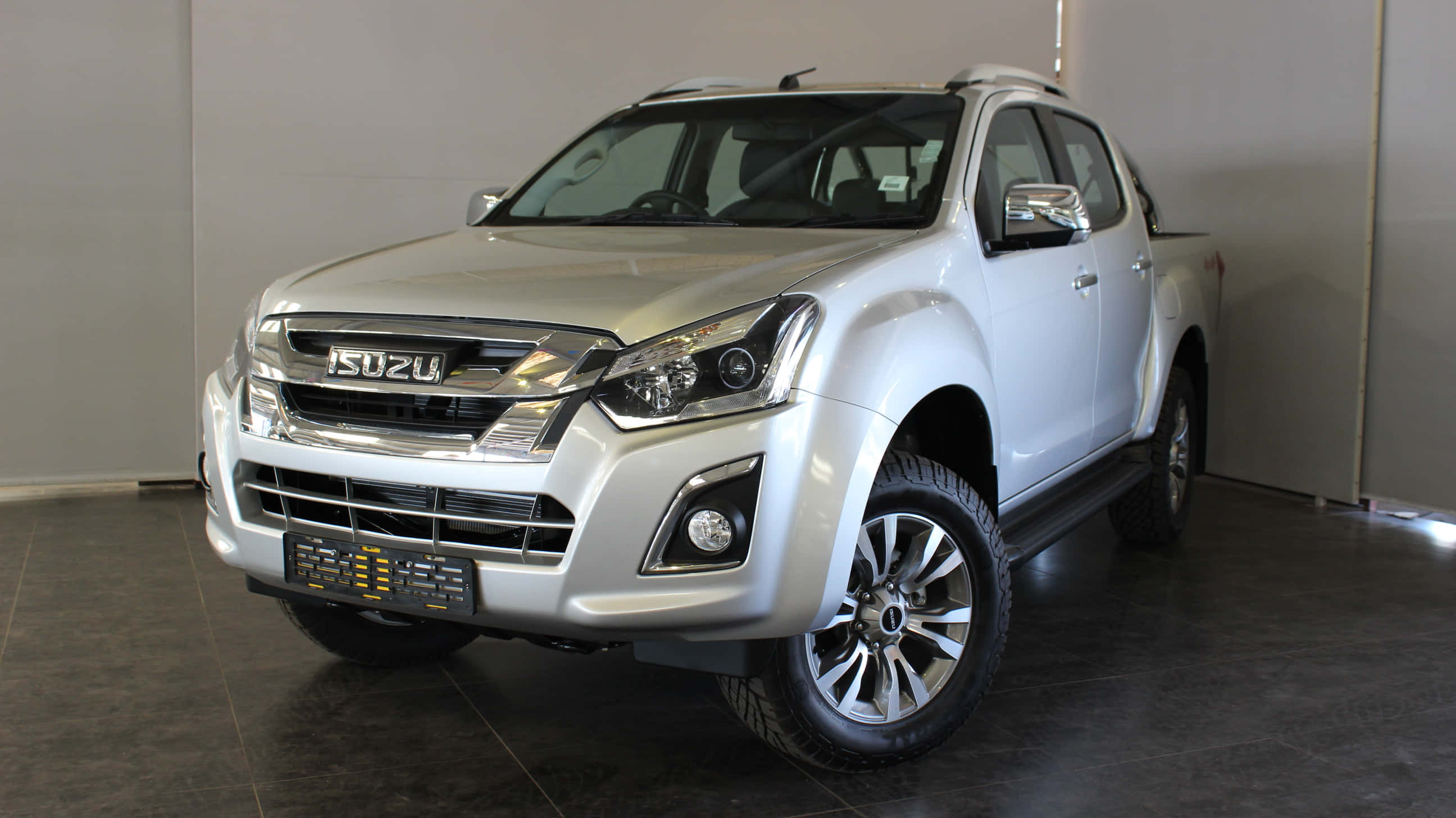 Isuzu 桌布 壁紙 — 一輛時尚的銀色五十鈴皮卡在現代展廳中展示，地板拋光，牆壁中性。