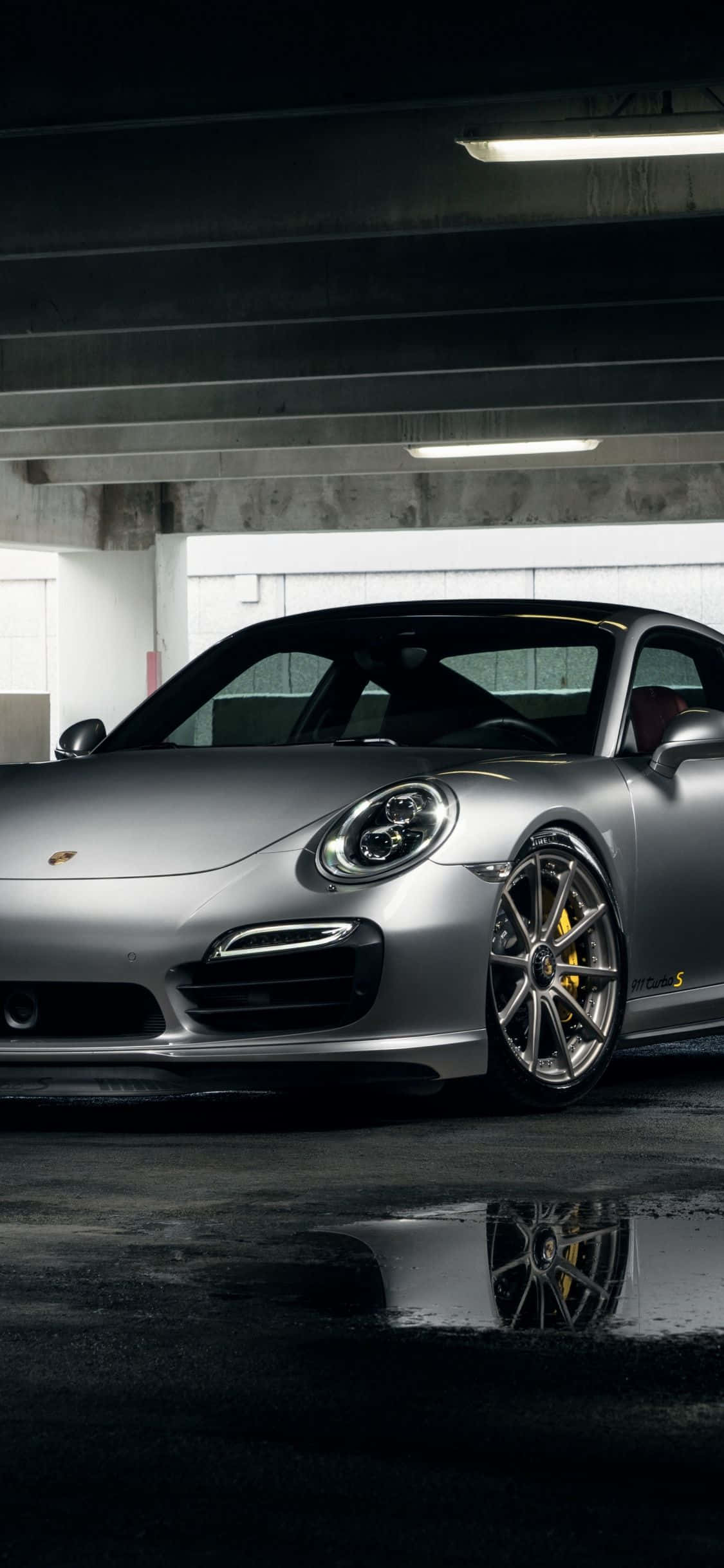 Porsche iPhone 桌布 壁紙 — 一輛時尚的銀色保時捷911 GT3 S停放在光線昏暗的地下停車場，濕漉漉的混凝土反射著車輪。