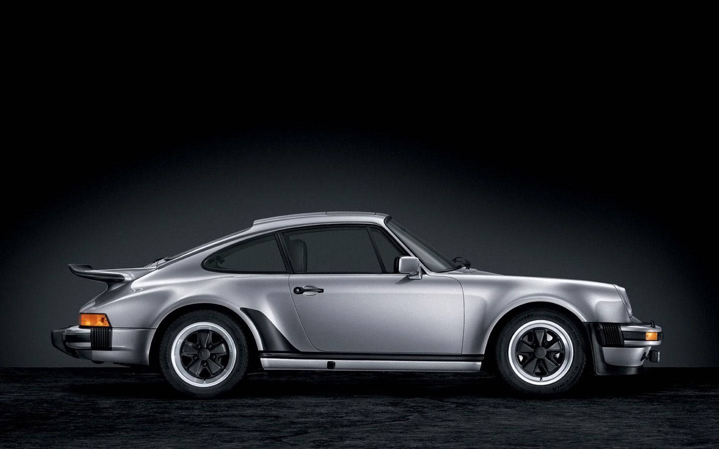 保時捷 911 桌布 壁紙 — 一輛時尚的銀色保時捷911 Turbo跑車在黑暗的攝影棚背景下以側面輪廓展示，配以戲劇性燈光。