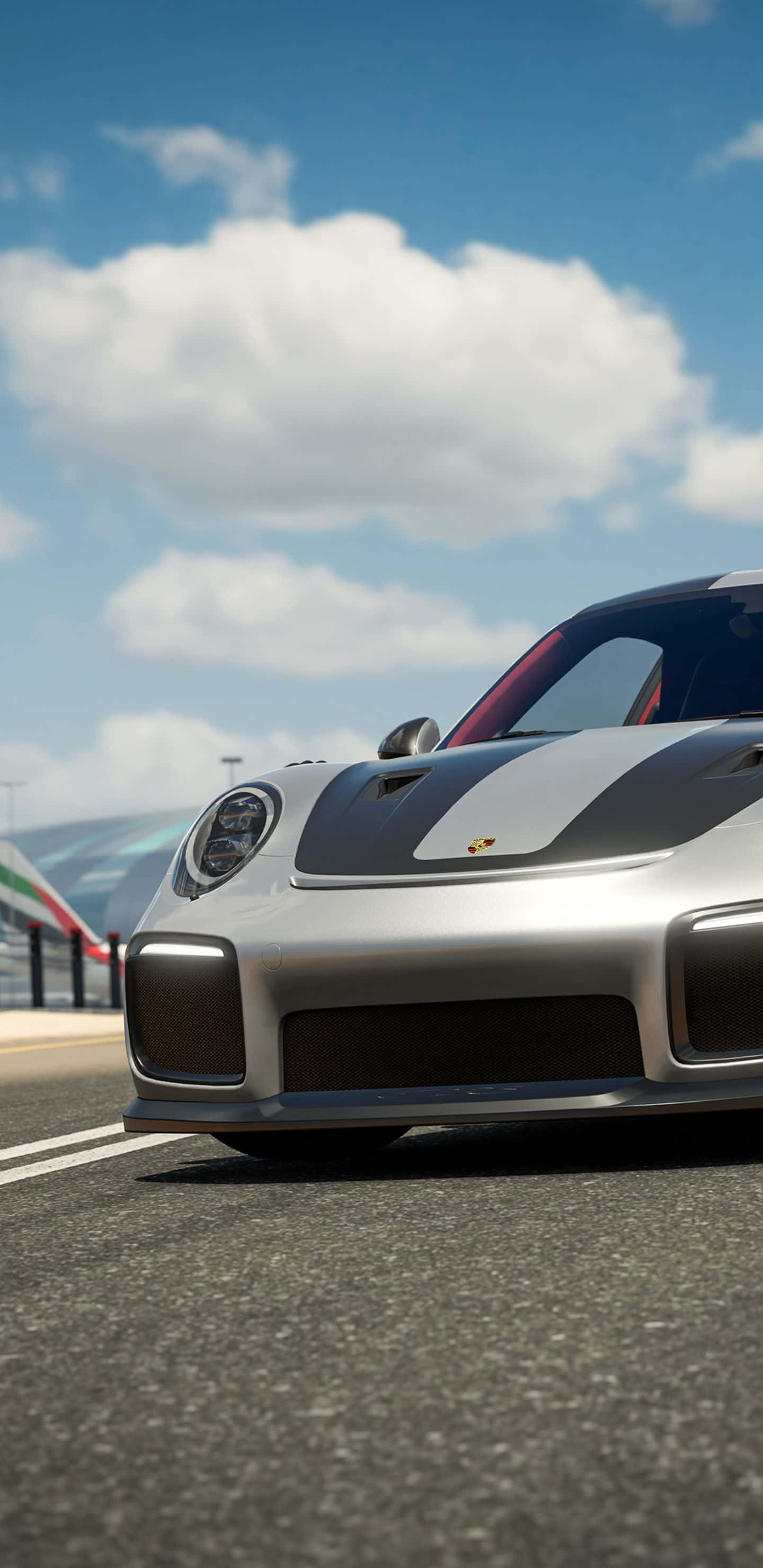 Pixel 3xl Forza Motorsport 7 桌布 壁紙 — 一輛時尚的銀色保時捷跑車帶有黑色賽車條紋，在晴朗藍天和蓬鬆白雲下沿著賽道飛馳。