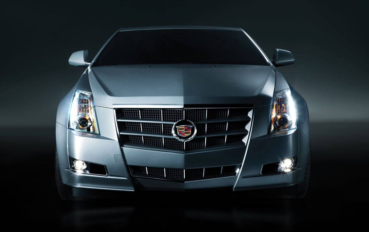 Cadillac 桌布 壁紙 — 一輛時尚的銀色凱迪拉克汽車正面視圖，帶有發光車頭燈，背景為深色工作室。