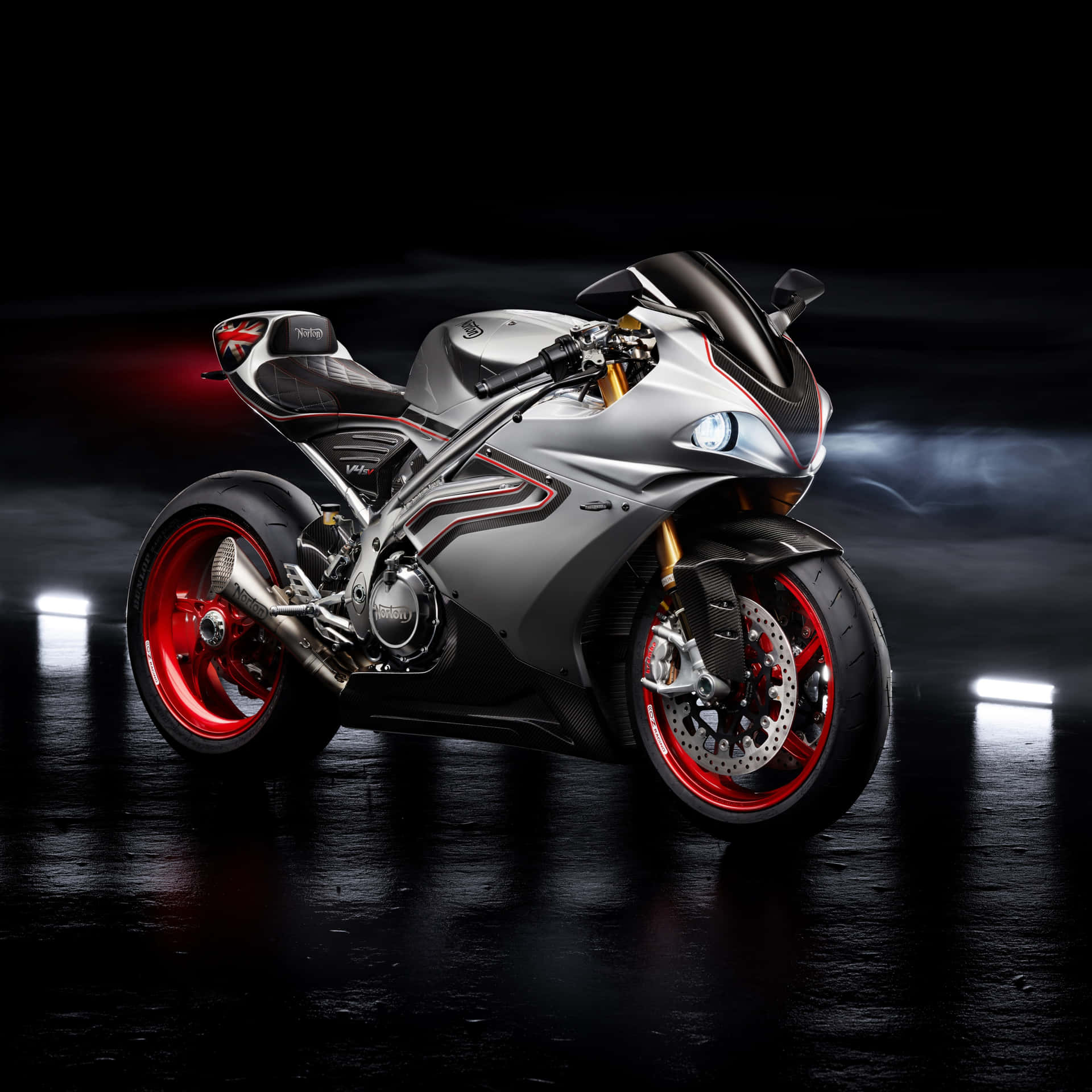 Superbike 桌布 壁紙 — 一輛時尚的銀色和紅色運動摩托車，帶有碳纖維飾件，在黑暗、反光的攝影棚地板上，被發光的聚光燈戲劇性地照亮。