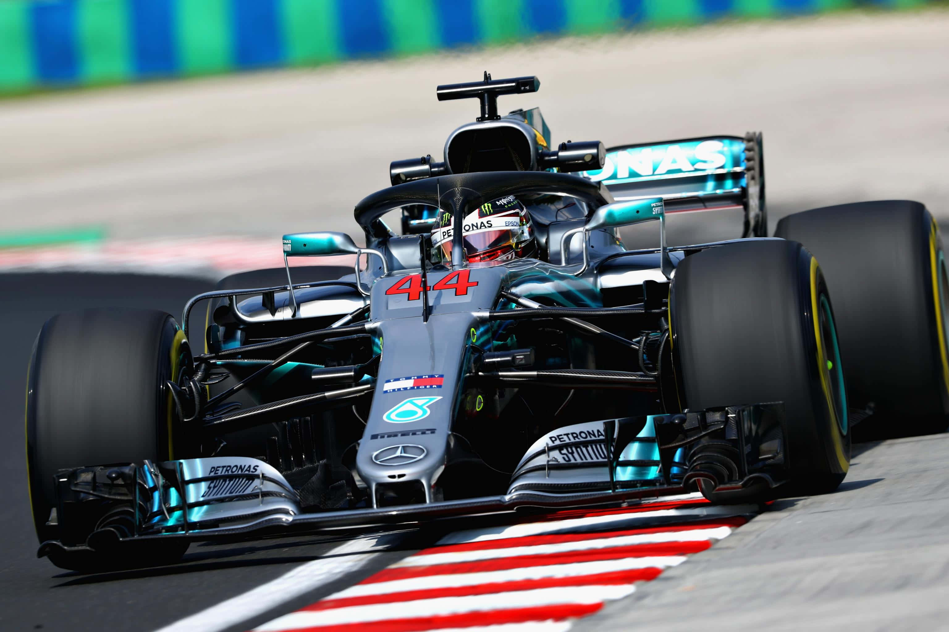 F1 2018 桌布 壁紙 — 一輛時尚的銀色和藍綠色一級方程式賽車，編號44，在明亮的日光下，在帶有紅色和白色路緣的賽道上奔馳。